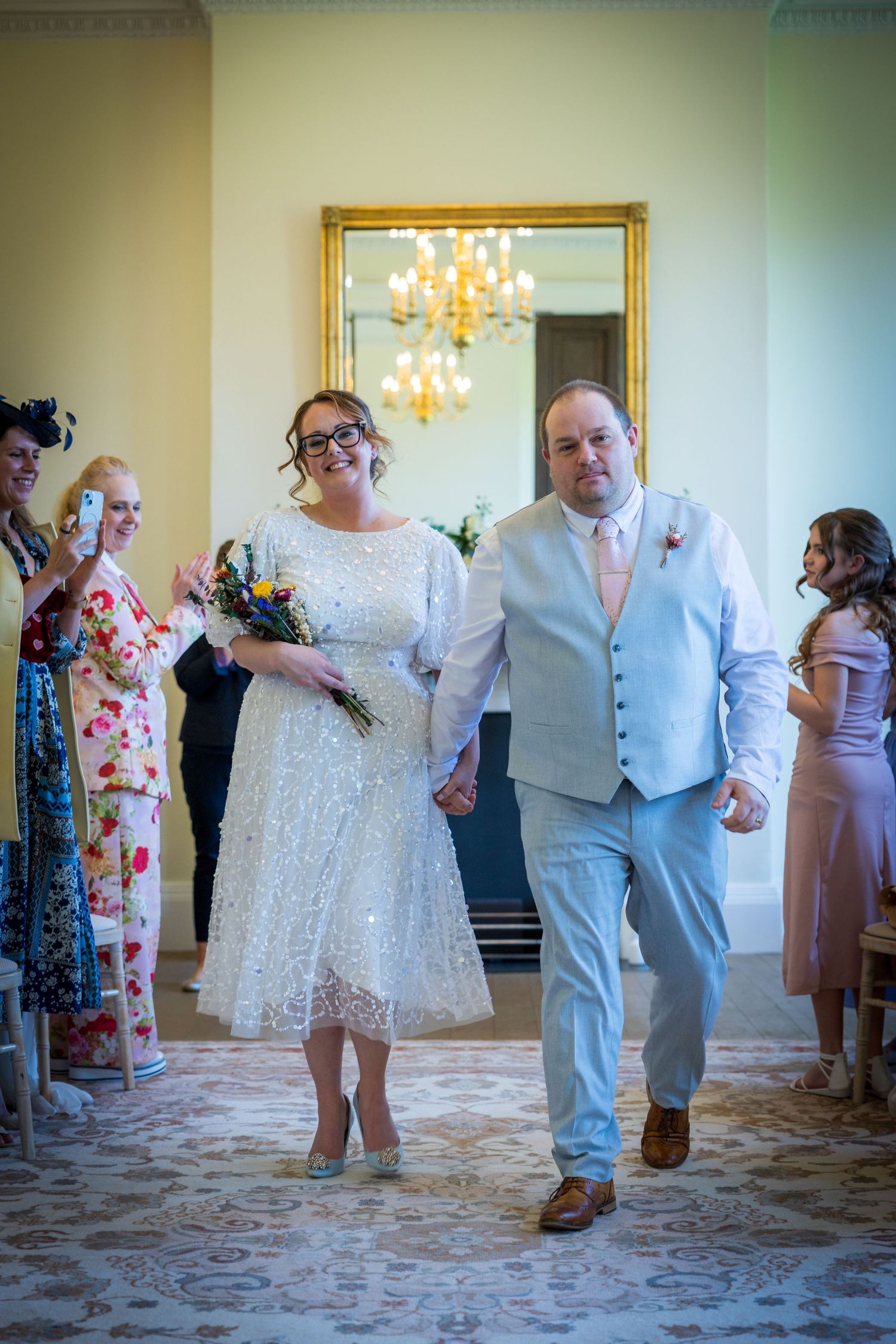 Newlyweds walk down aisle at The Story, Durham; guests smile and clap in bright, elegant room.