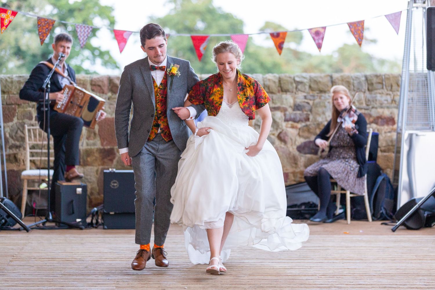 Bride and groom dance to traditional music at rustic North East UK wedding, lively celebration with folk band and colourful decor