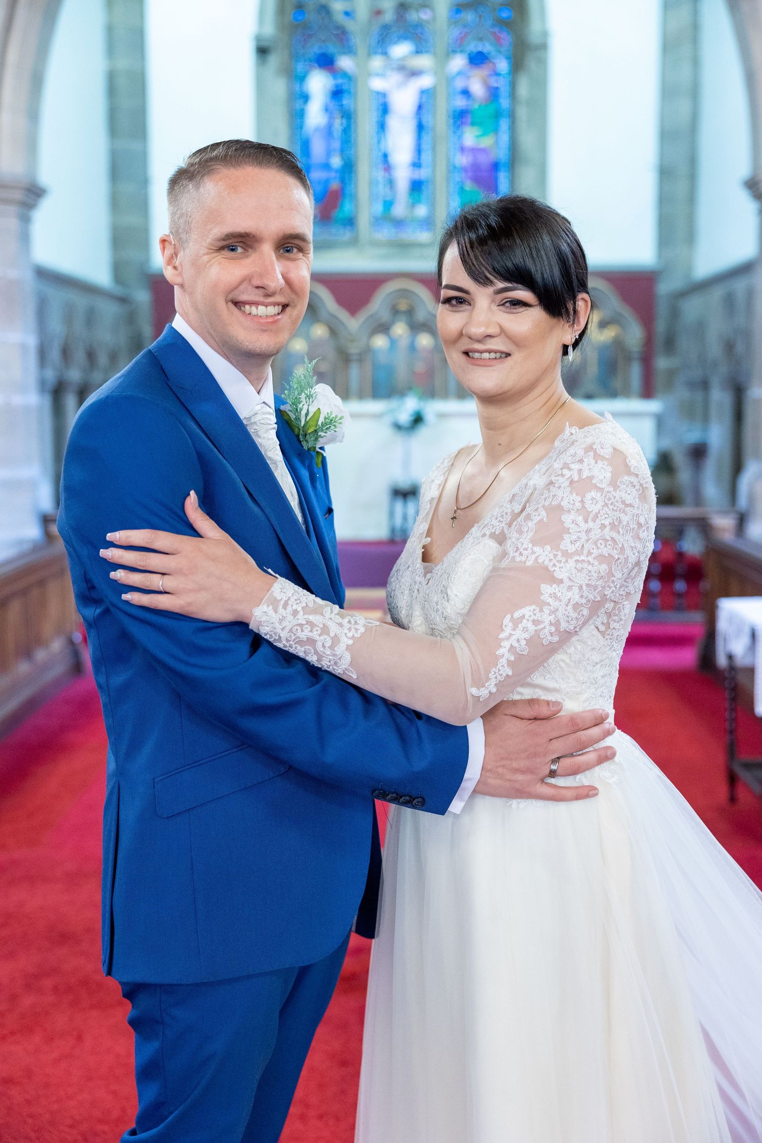 Bride and groom portrait in church, elegant wedding couple embracing on aisle with stained glass, classic ceremony setting.