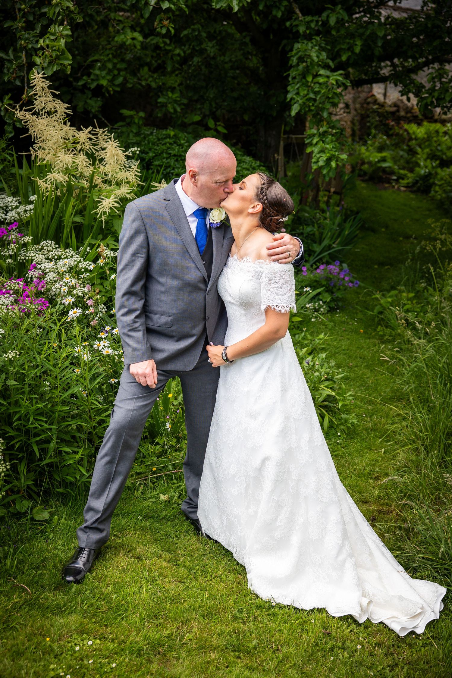 Bride and groom share a romantic kiss in lush garden, natural wedding portrait, outdoor venue, intimate moment captured in beautiful greener