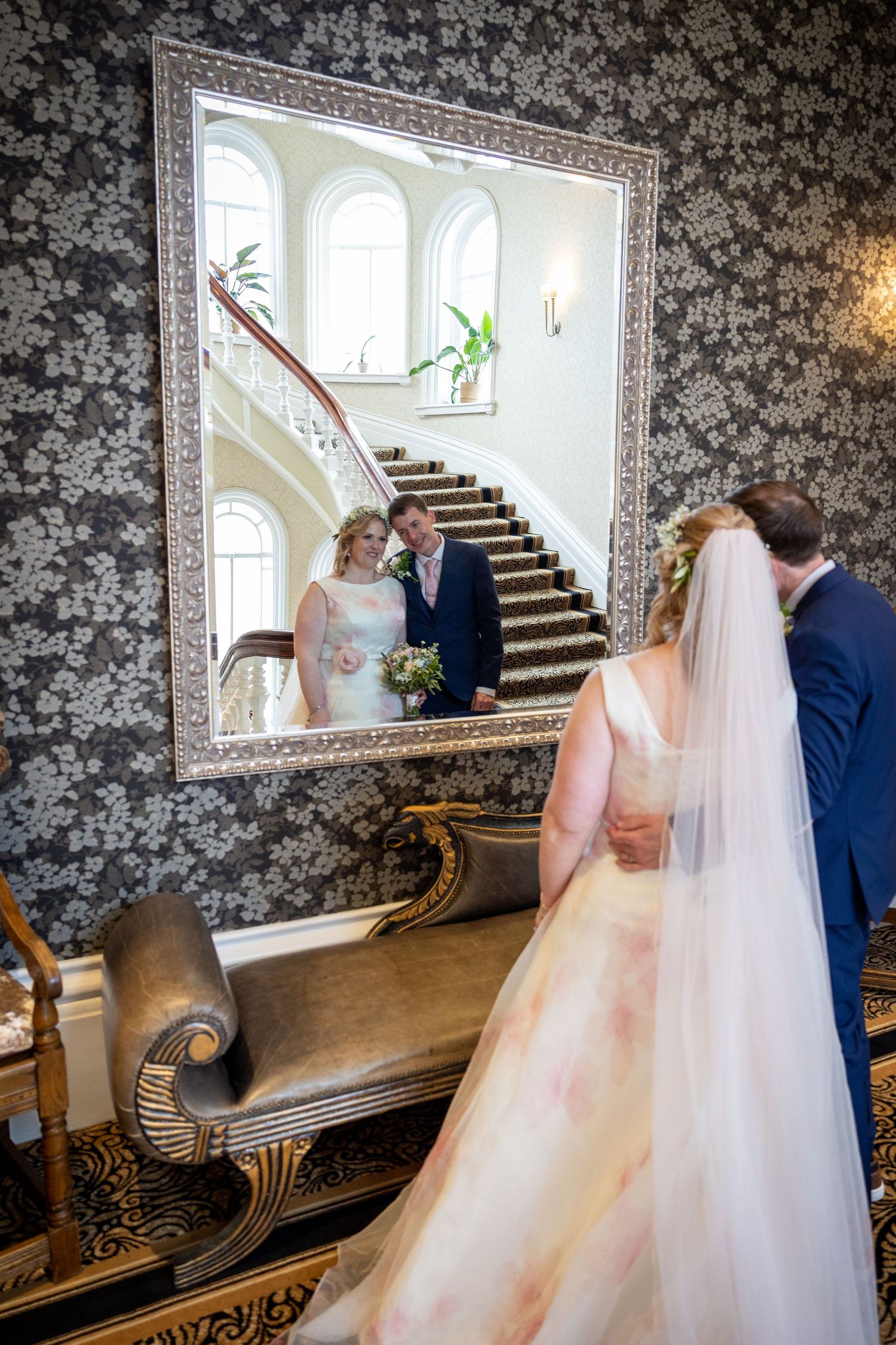 Bride and groom reflected in ornate mirror at The Grand Tynemouth, elegant staircase backdrop, romantic indoor wedding portrait