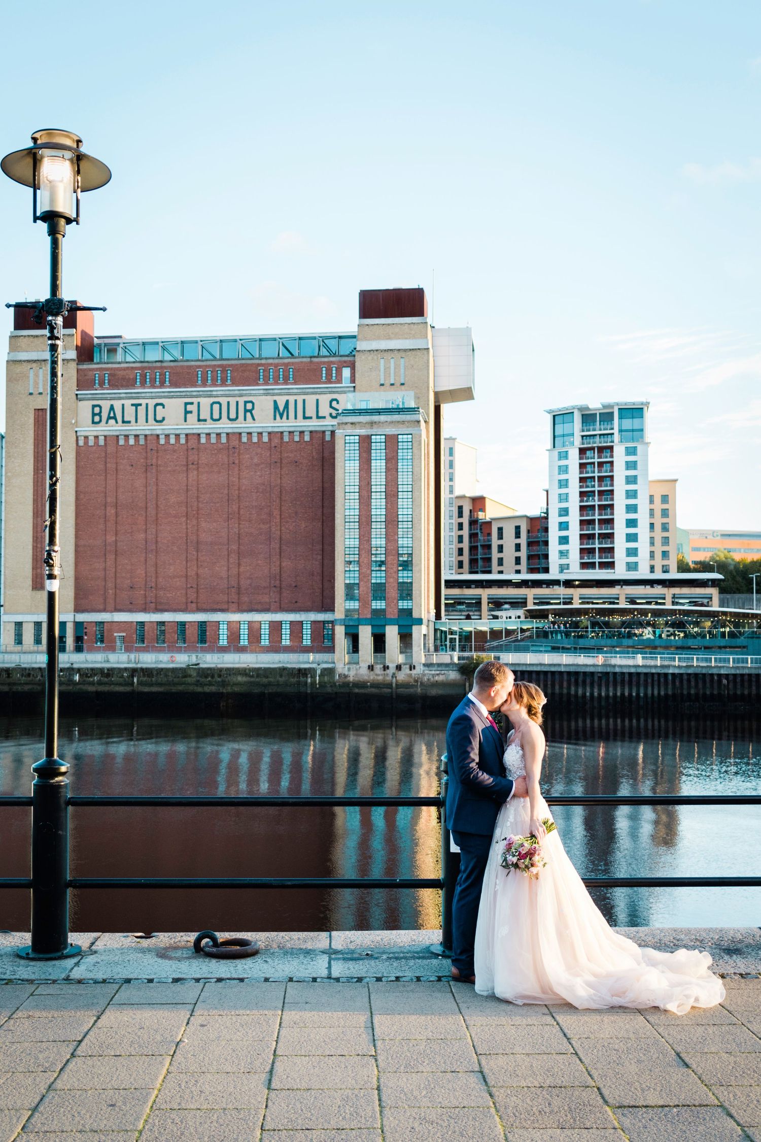 Couple kiss by the river at Baltic Flour Mills, Gateshead; modern cityscape and quayside setting.