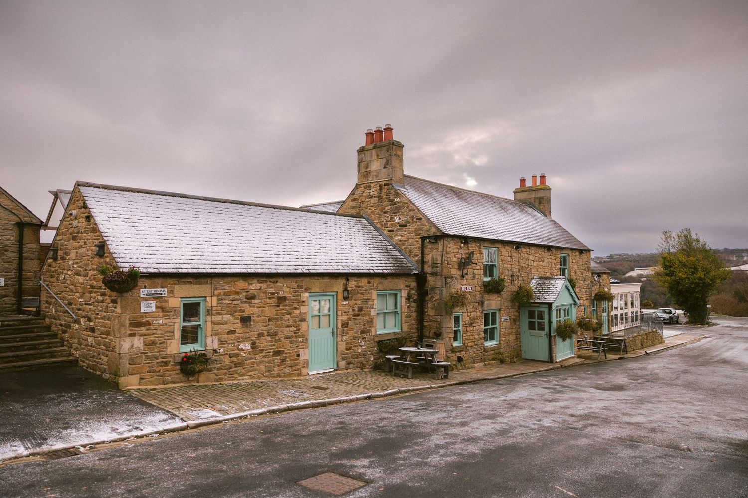 Rustic stone cottages with snowy roofs; charming countryside scene under cloudy winter sky.