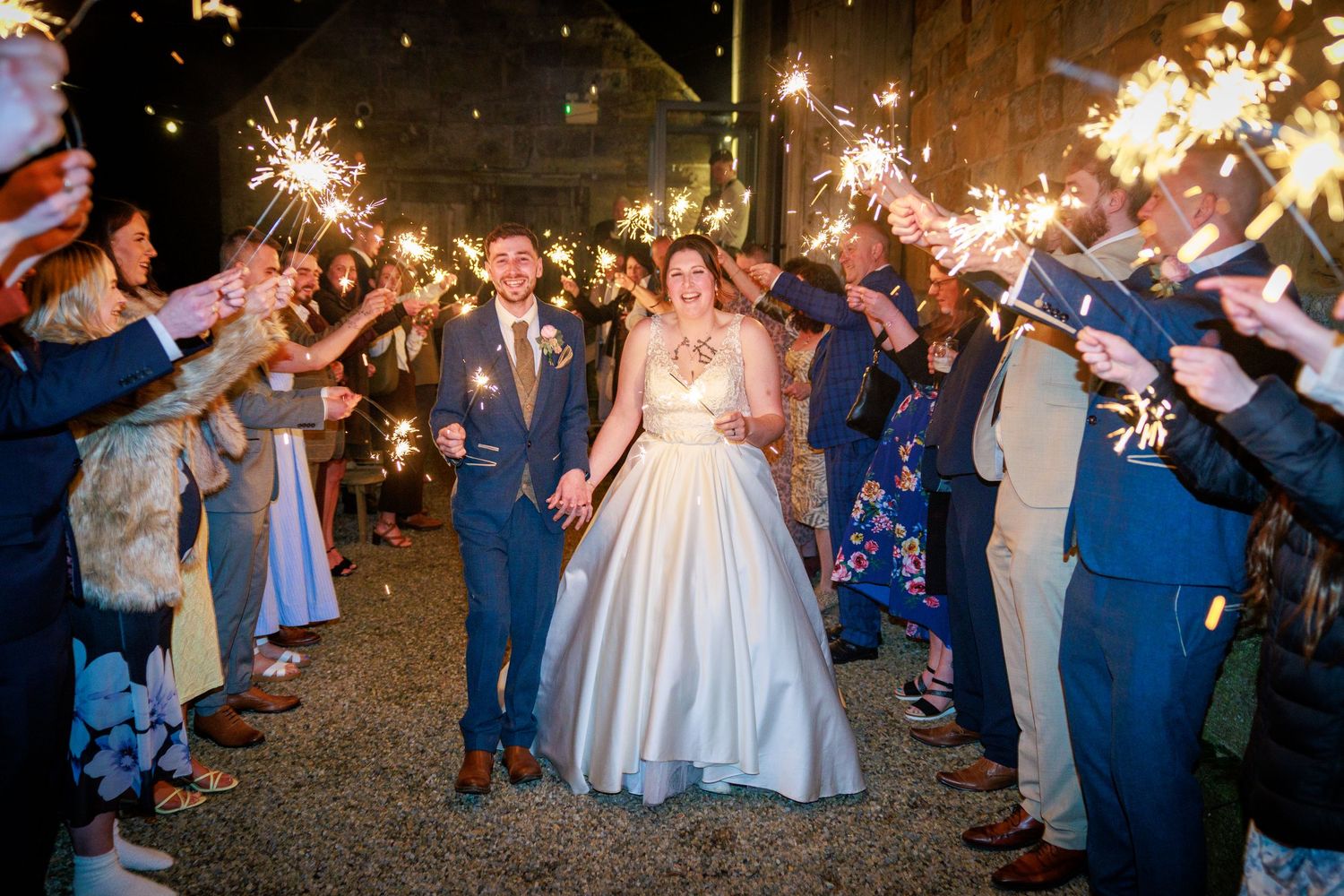 Sparkler exit at Danby Castle; newlyweds walk through cheering guests in a joyful nighttime send-off.