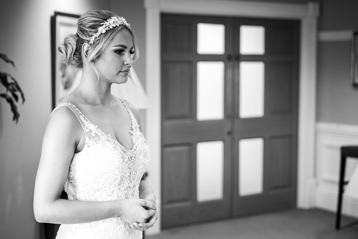 Bride waits in quiet moment; elegant black-and-white portrait with soft light and classic interior.