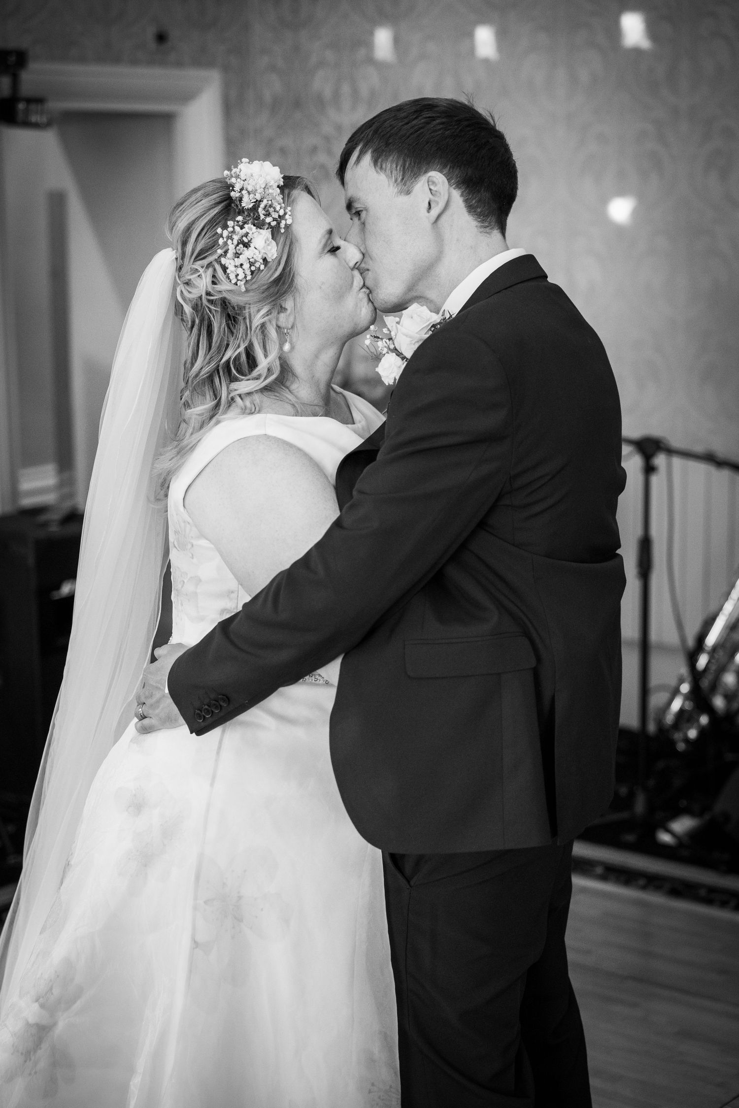 Bride and groom share first dance kiss, black and white wedding photo, romantic moment, emotional reception scene