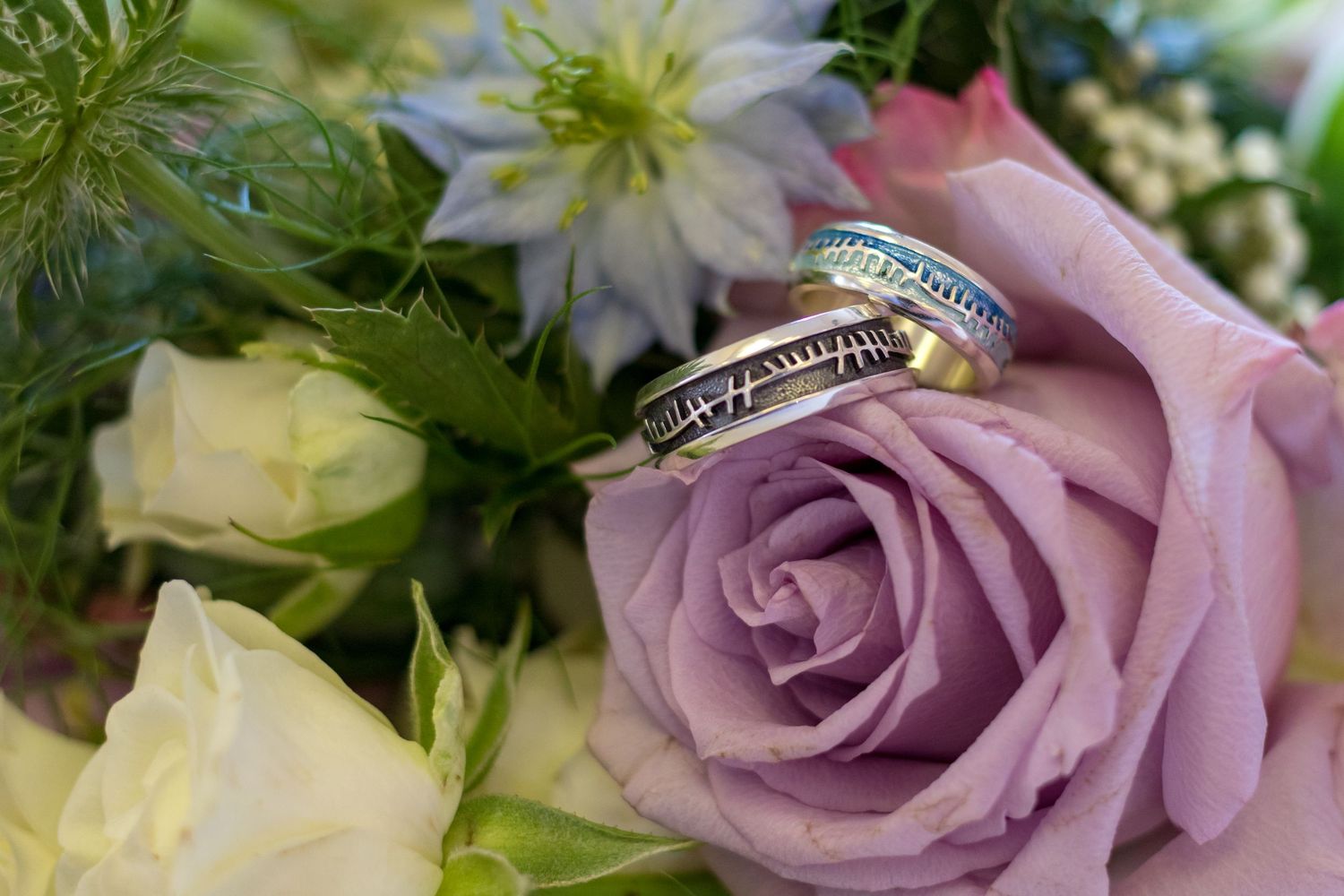 Close-up of wedding rings nestled in a bouquet; soft florals and pastel tones create a delicate, romantic detail shot.