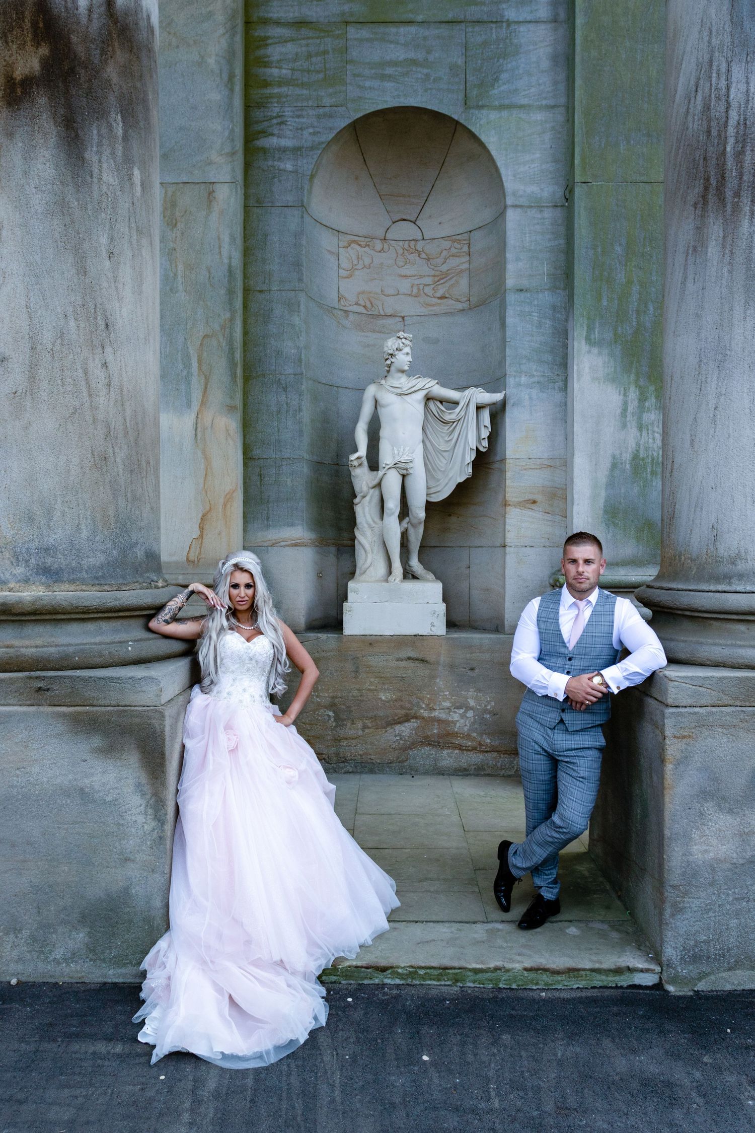 Couple pose at Wynyard Hall; dramatic architectural backdrop with classical statue and elegant styling.