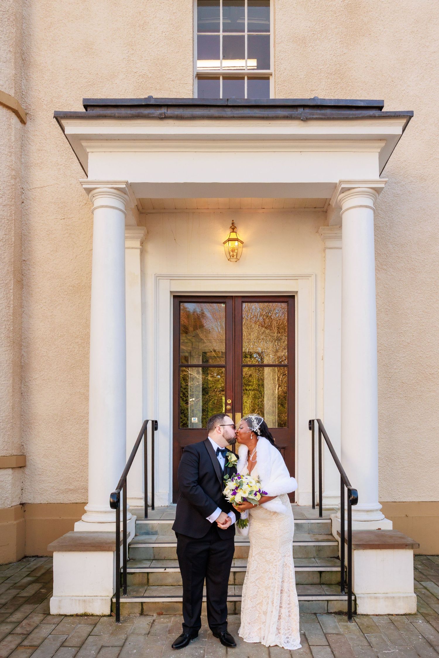 Couple share a kiss on steps at The Story, Durham; elegant entrance with columns behind.