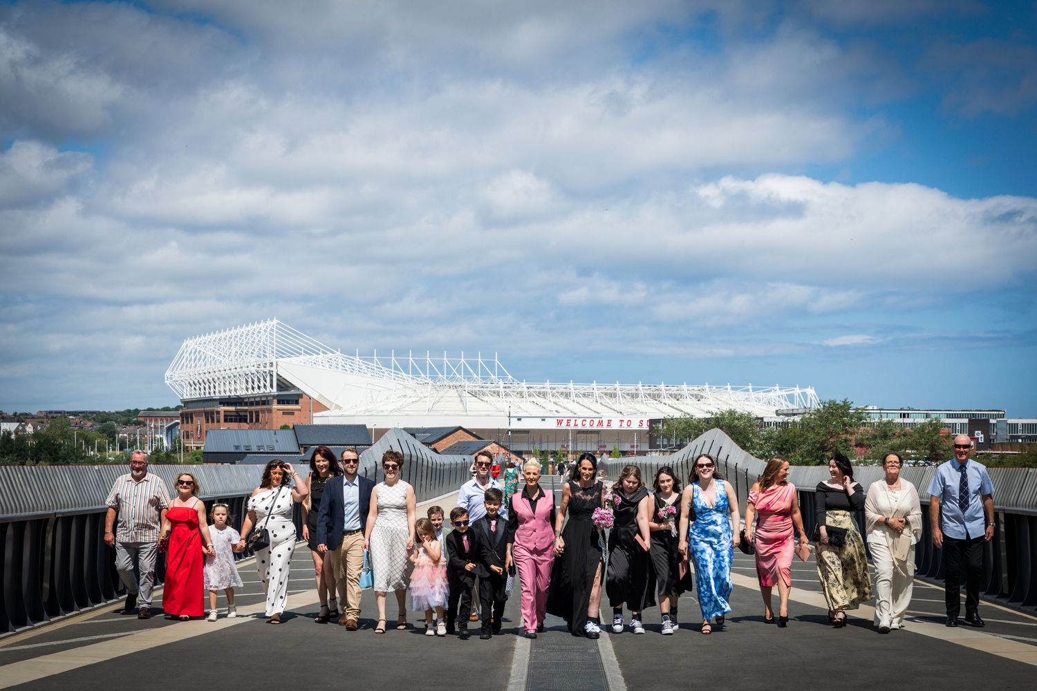 Wedding party gathered outside the Stadium of Light in Sunderland under a bright blue sky.