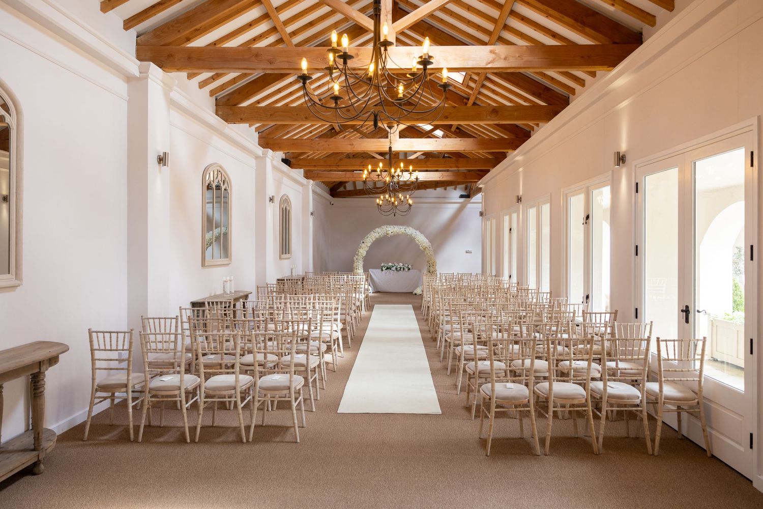 Elegant wedding ceremony room setup, rustic beams and chandeliers, aisle and floral arch, bright modern venue ready for guests