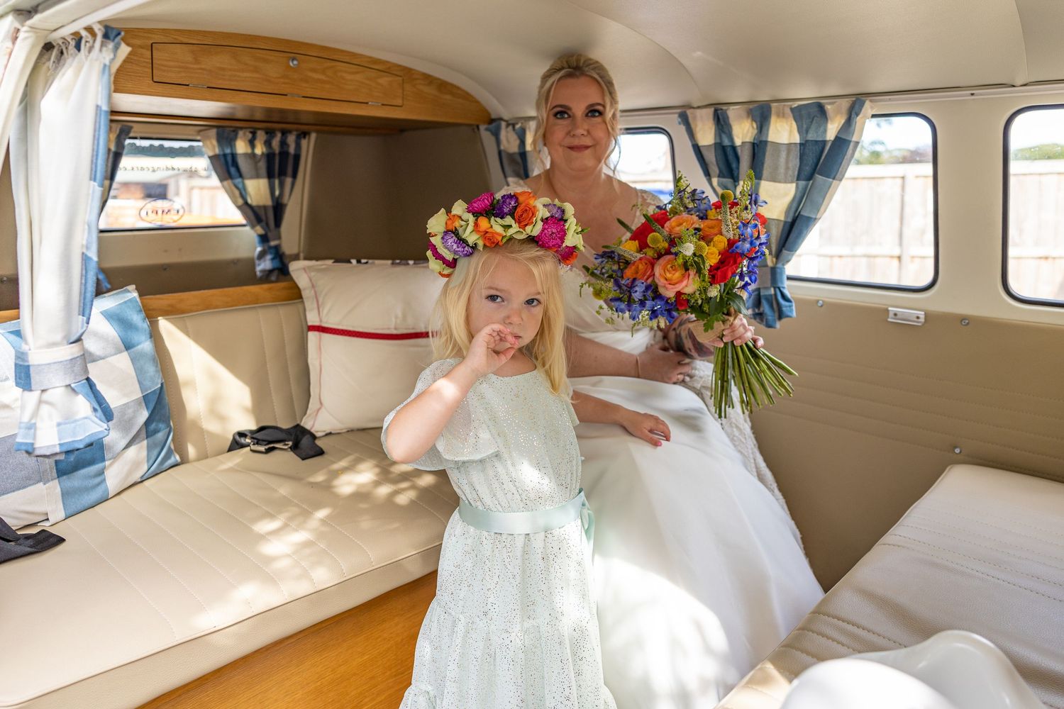Bride and flower girl inside vintage camper at The Gables, Escomb; bright, playful moment with colorful bouquets.