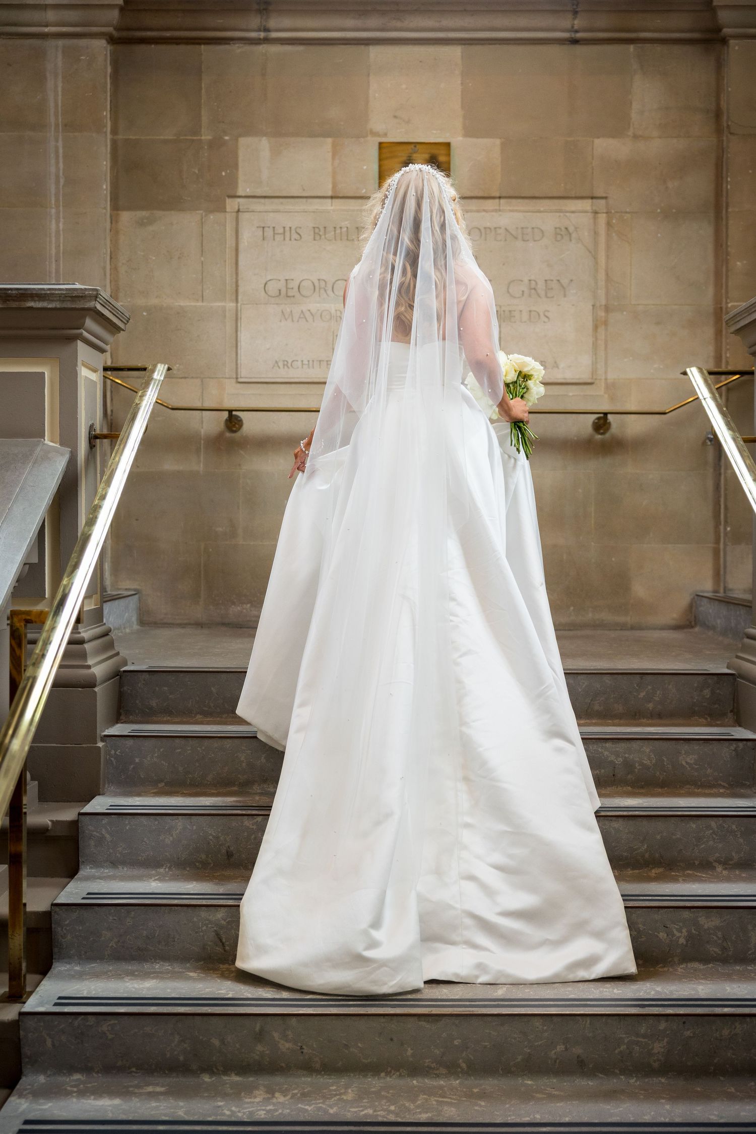 Bride descends staircase at South Shields Registry Office; elegant stone and stained glass backdrop.