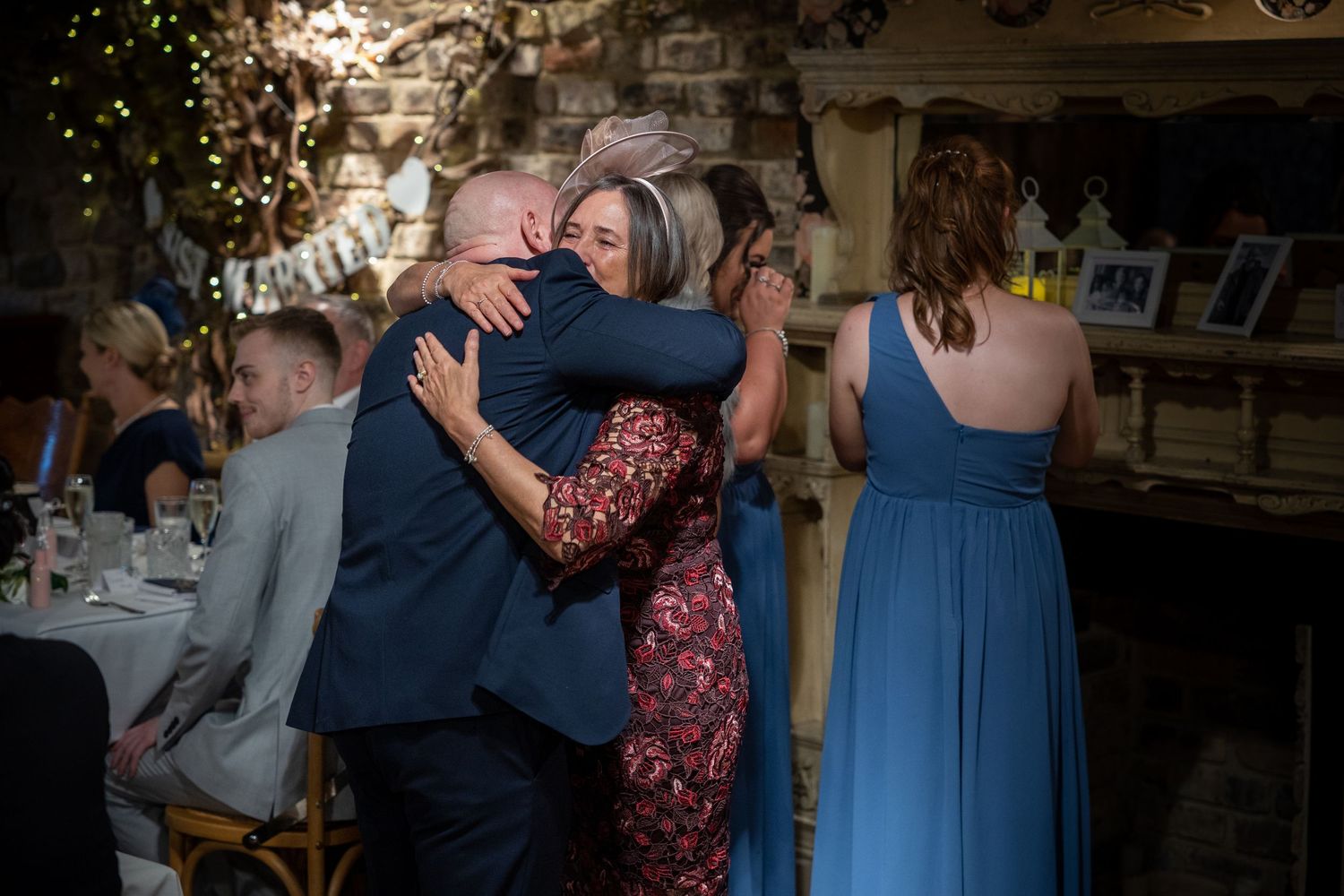 Emotional embrace at the reception; heartfelt moment between guests amid warm lighting and lively celebration.