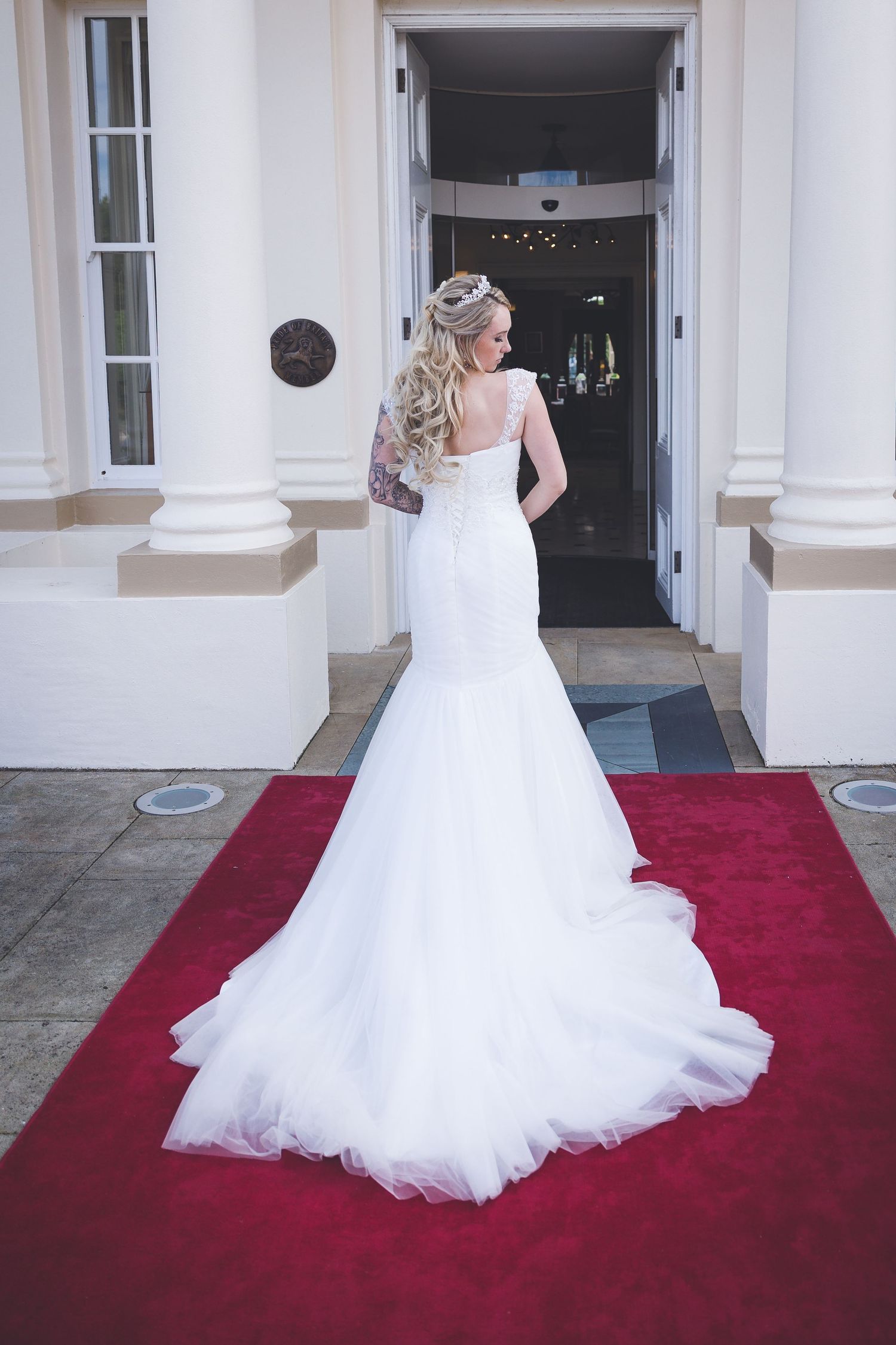 Bride in elegant wedding dress at Seaham Hall entrance, back view on red carpet, stylish bridal portrait at luxury venue.