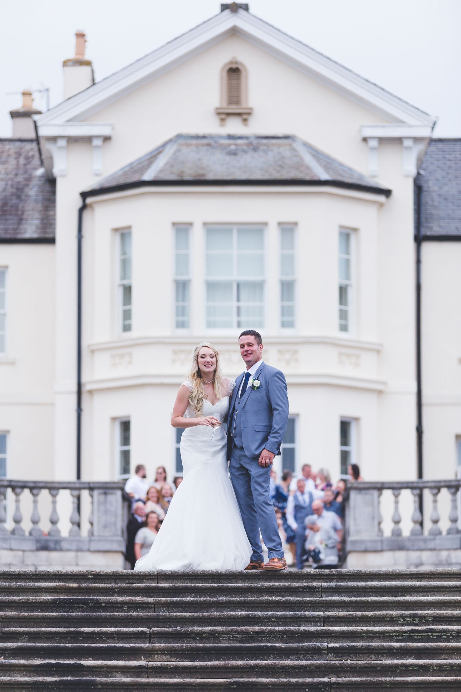 Couple pose on steps at Seaham Hall; elegant façade and gathered guests create a timeless wedding portrait.