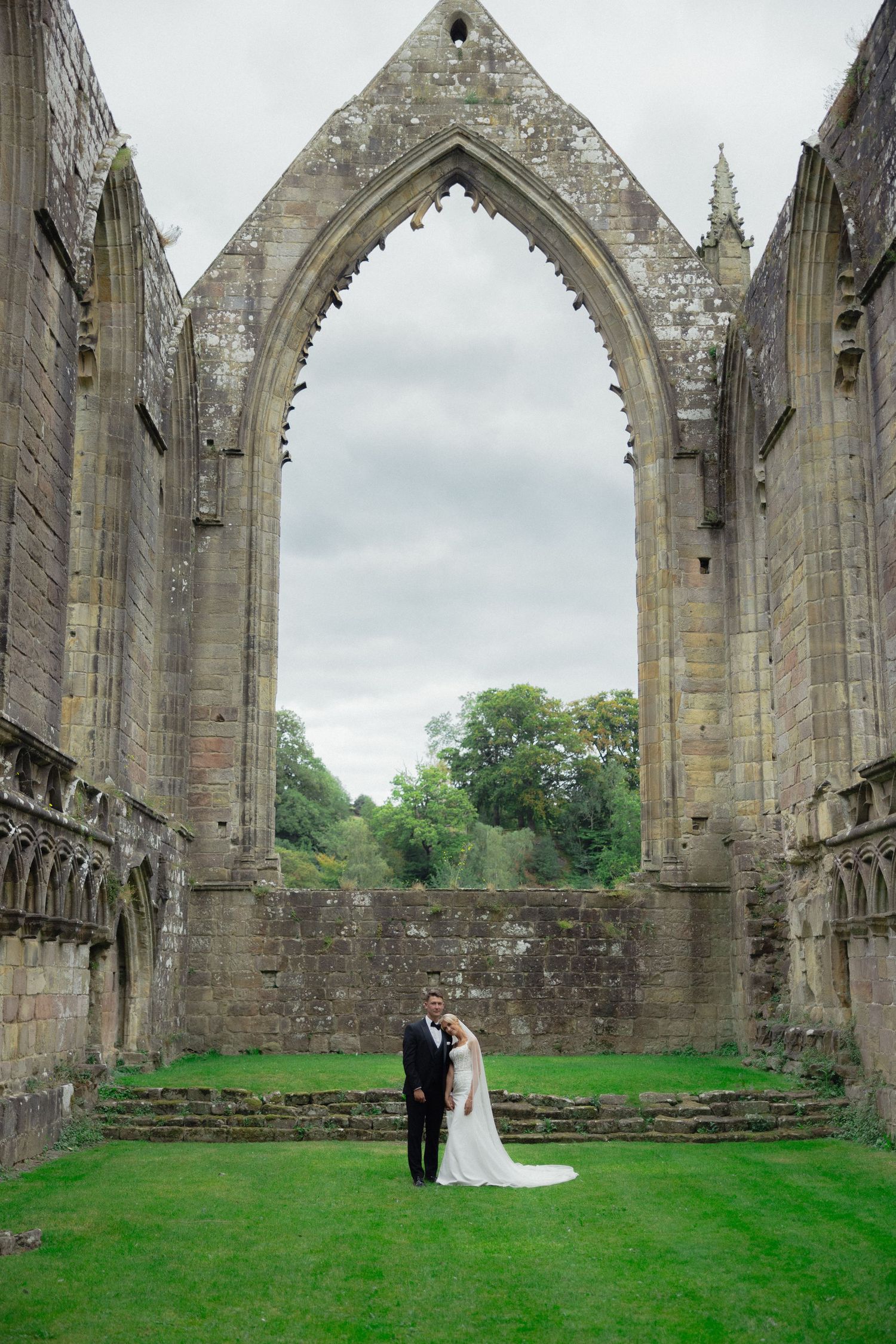 Wedding photography in a dramatic stone cathedral ruins with towering gothic arches and green grass.