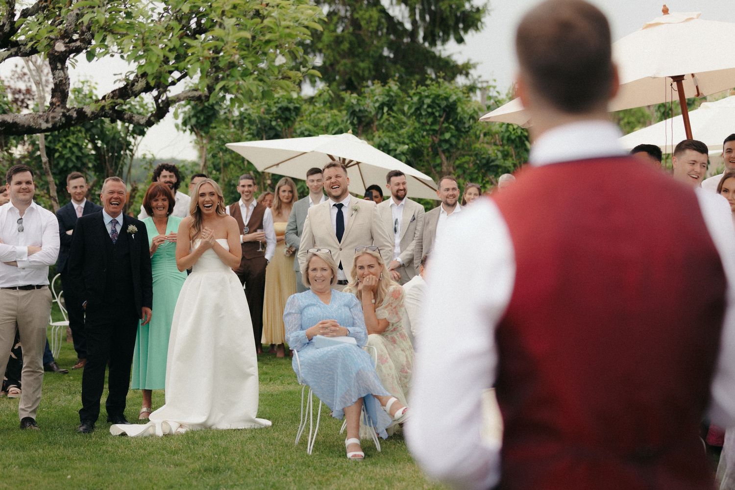Guests mingle at an outdoor garden wedding with white umbrellas and greenery.