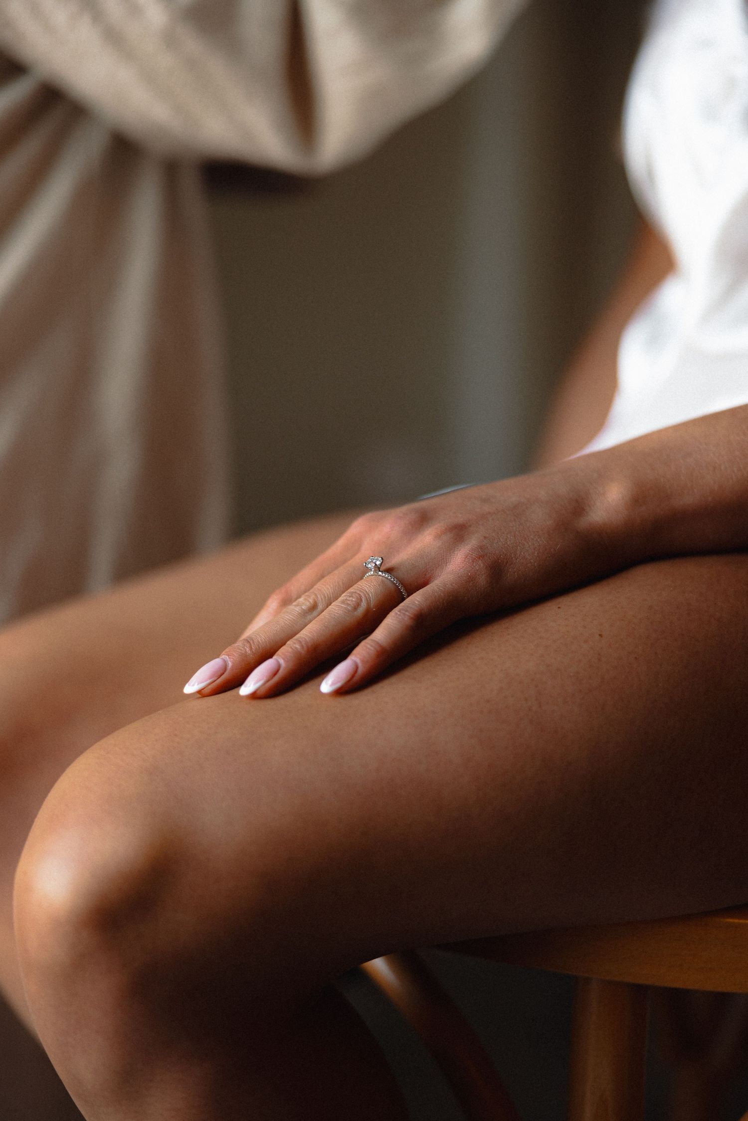 Close-up of hand with engagement ring resting on leg in natural light.