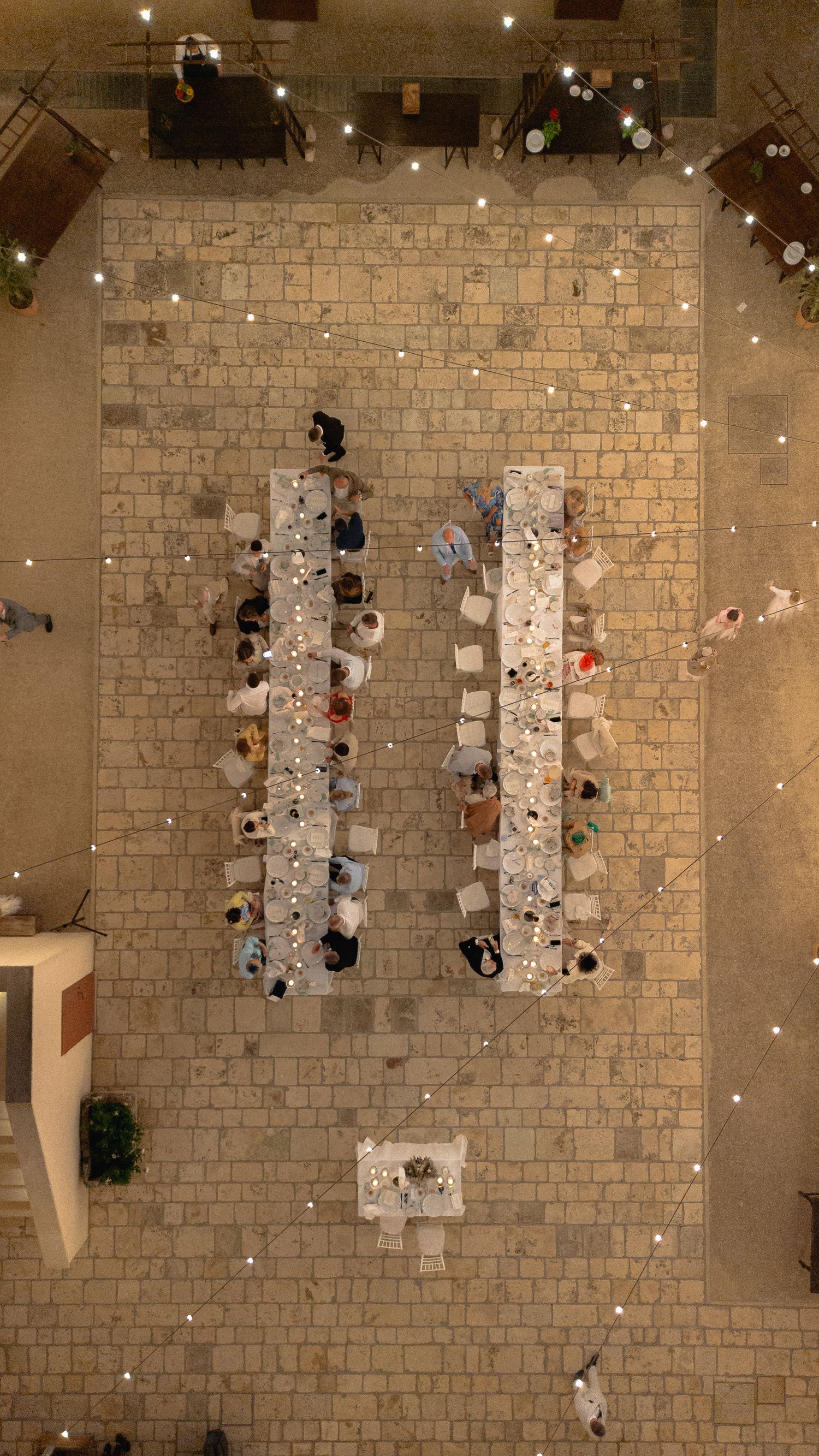 Aerial view of wedding reception tables arranged on stone patio with string lights overhead.