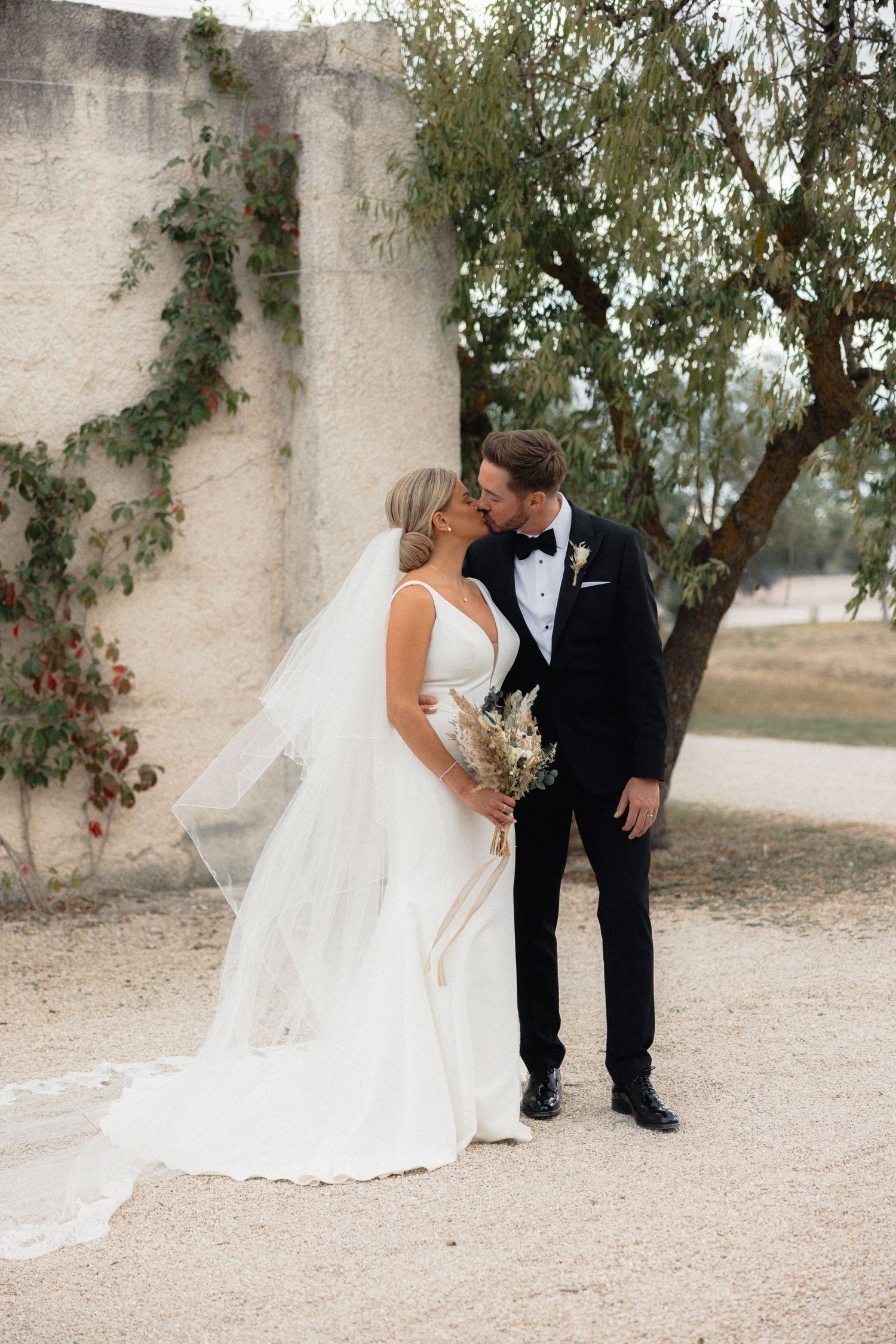 Elegant wedding portraits captured against a textured wall with natural foliage.
