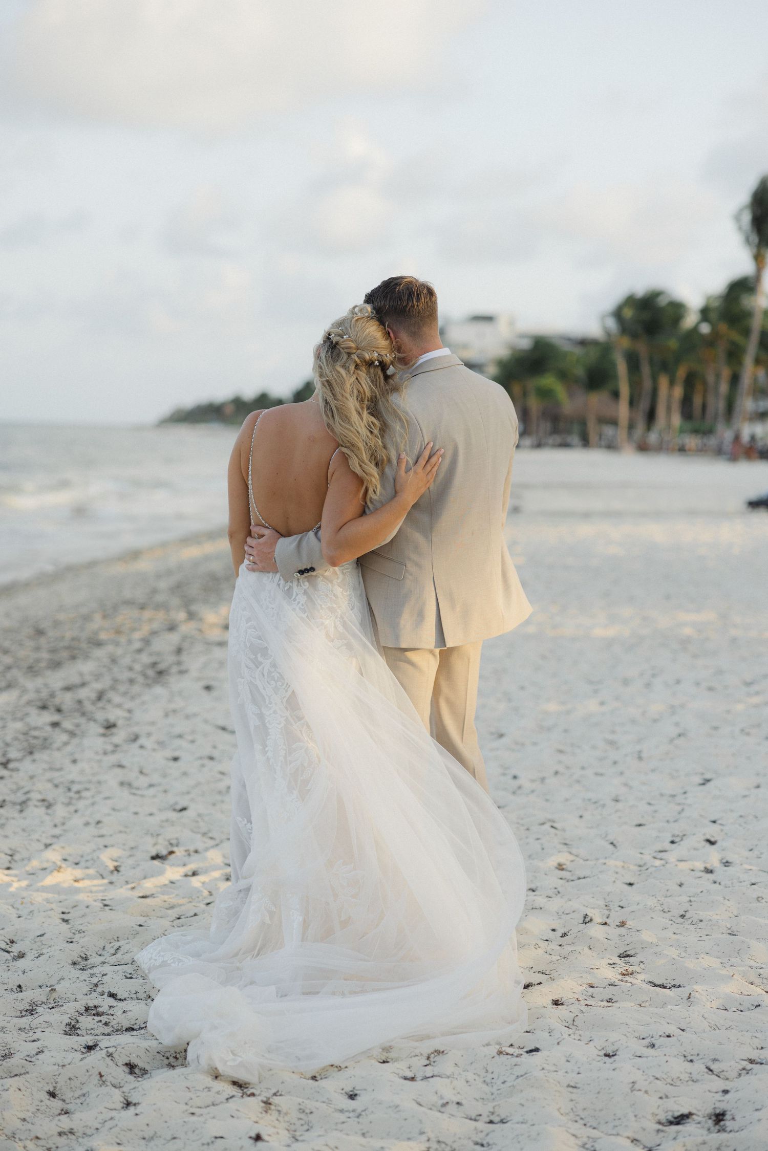 Newlyweds embrace while looking at ocean view on sandy beach.