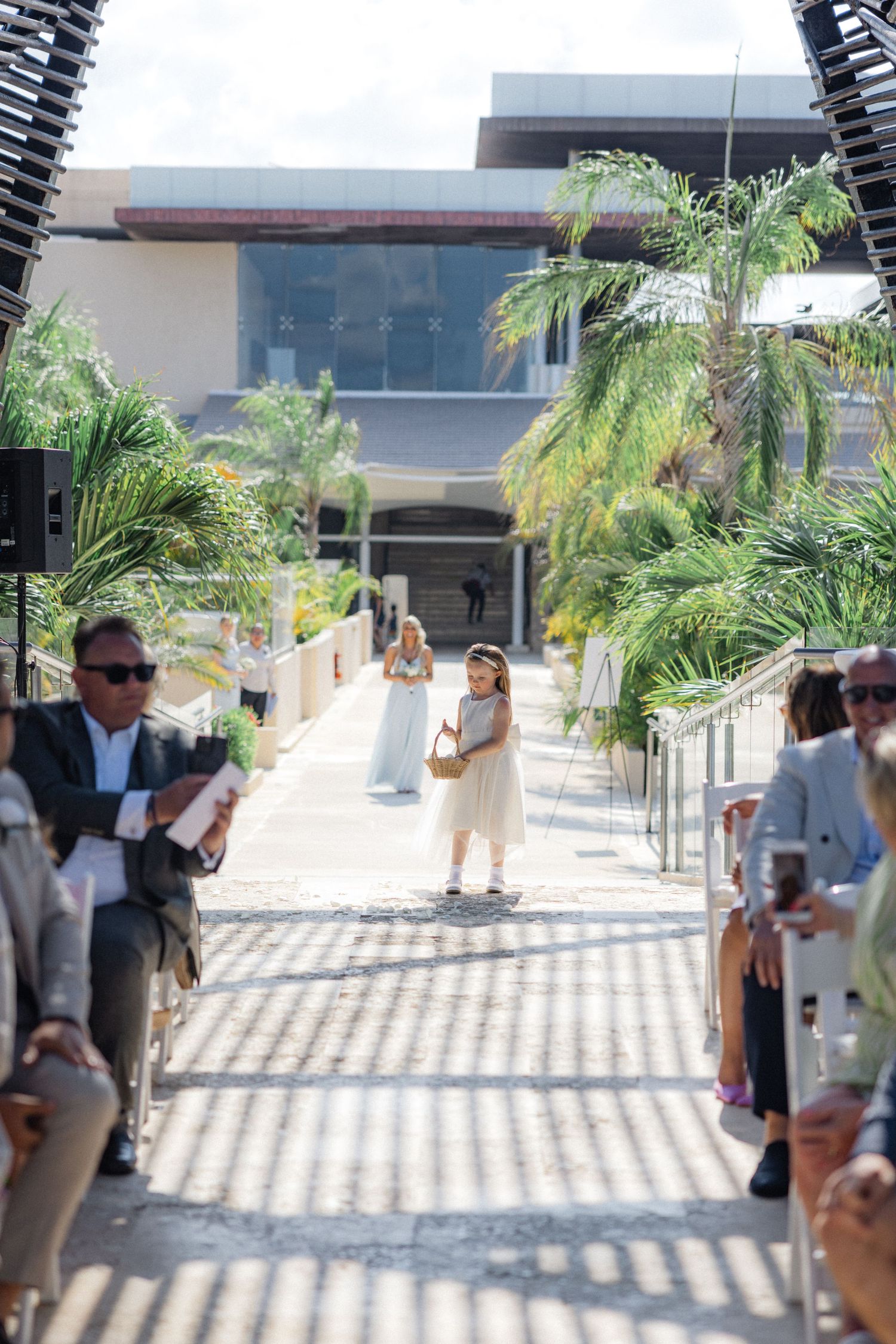 Wedding party poses under palm trees and modern architectural elements in bright sunlight.