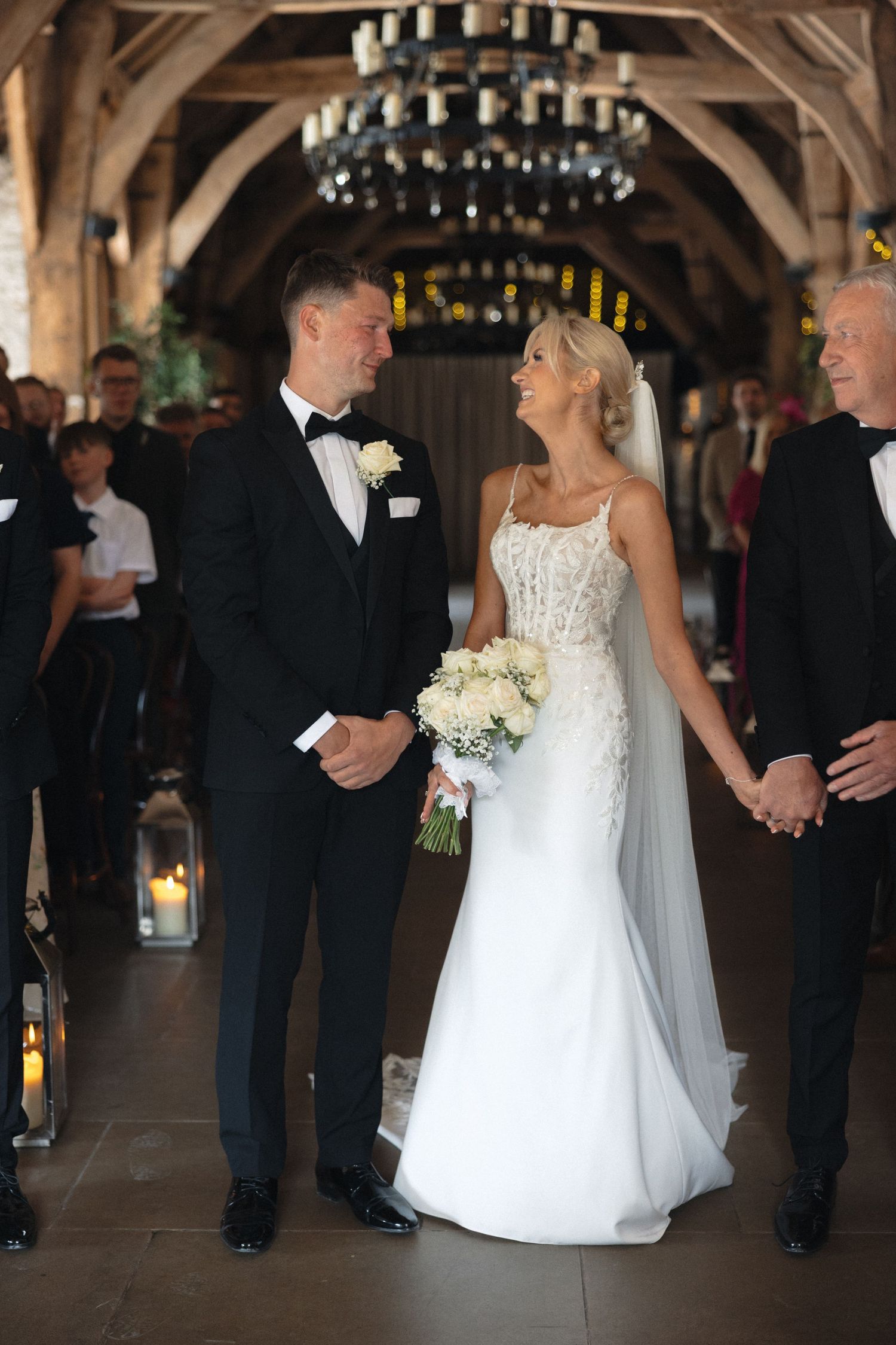 Wedding ceremony procession in elegant barn venue with hanging chandeliers.