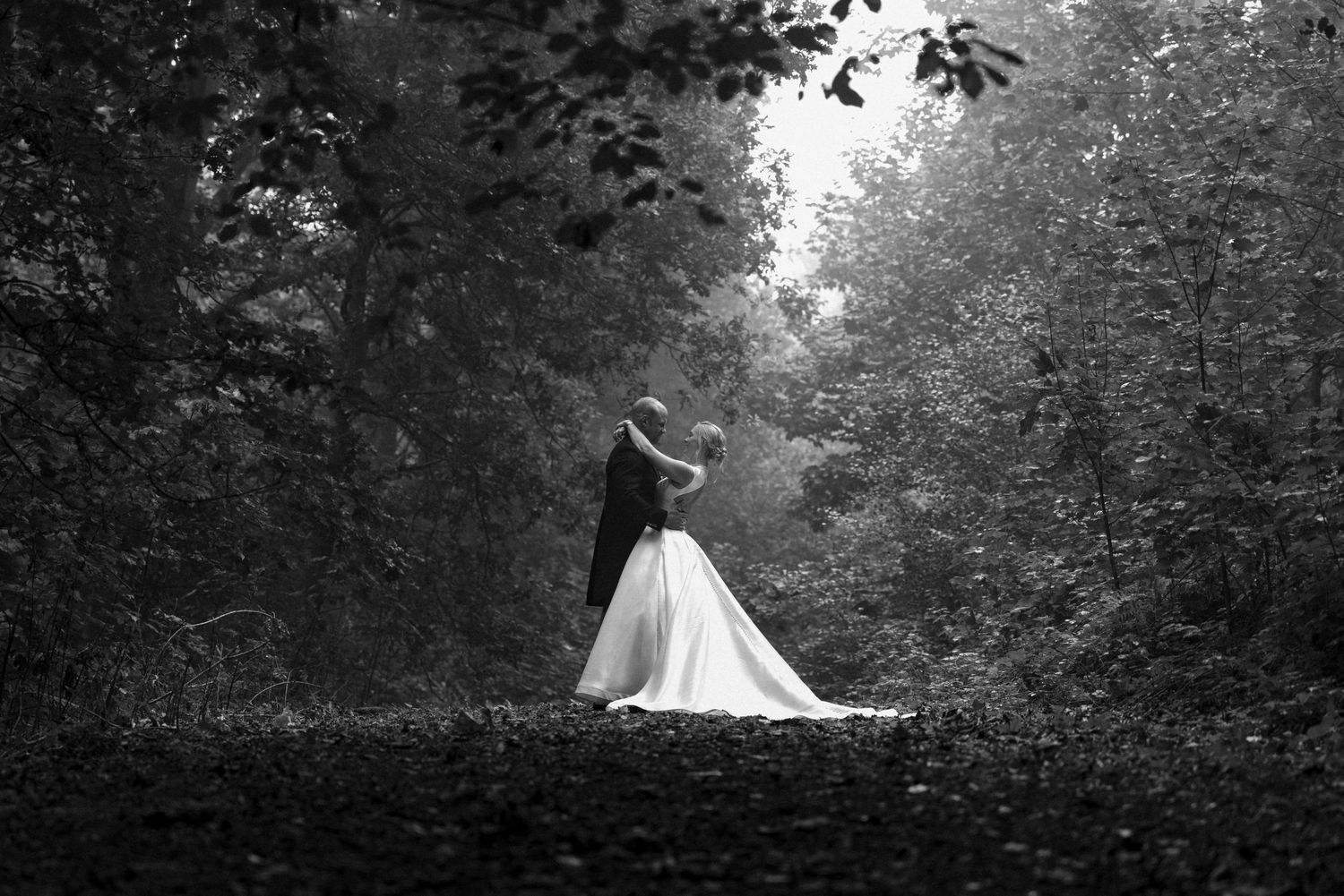 Ethereal forest wedding scene with white dress contrasting against dark trees.