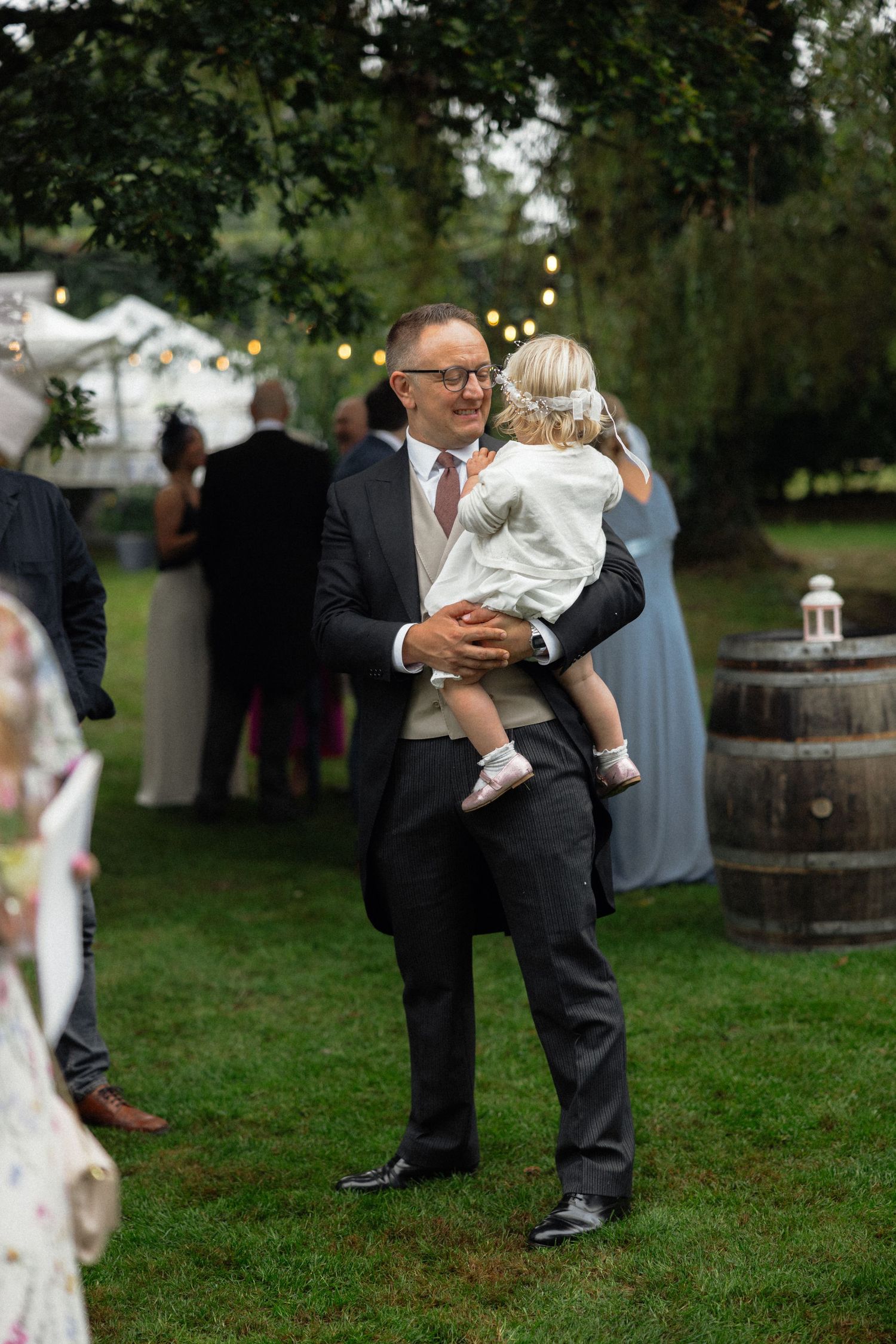 Wedding celebration on grass with guests mingling around rustic barrel decor.