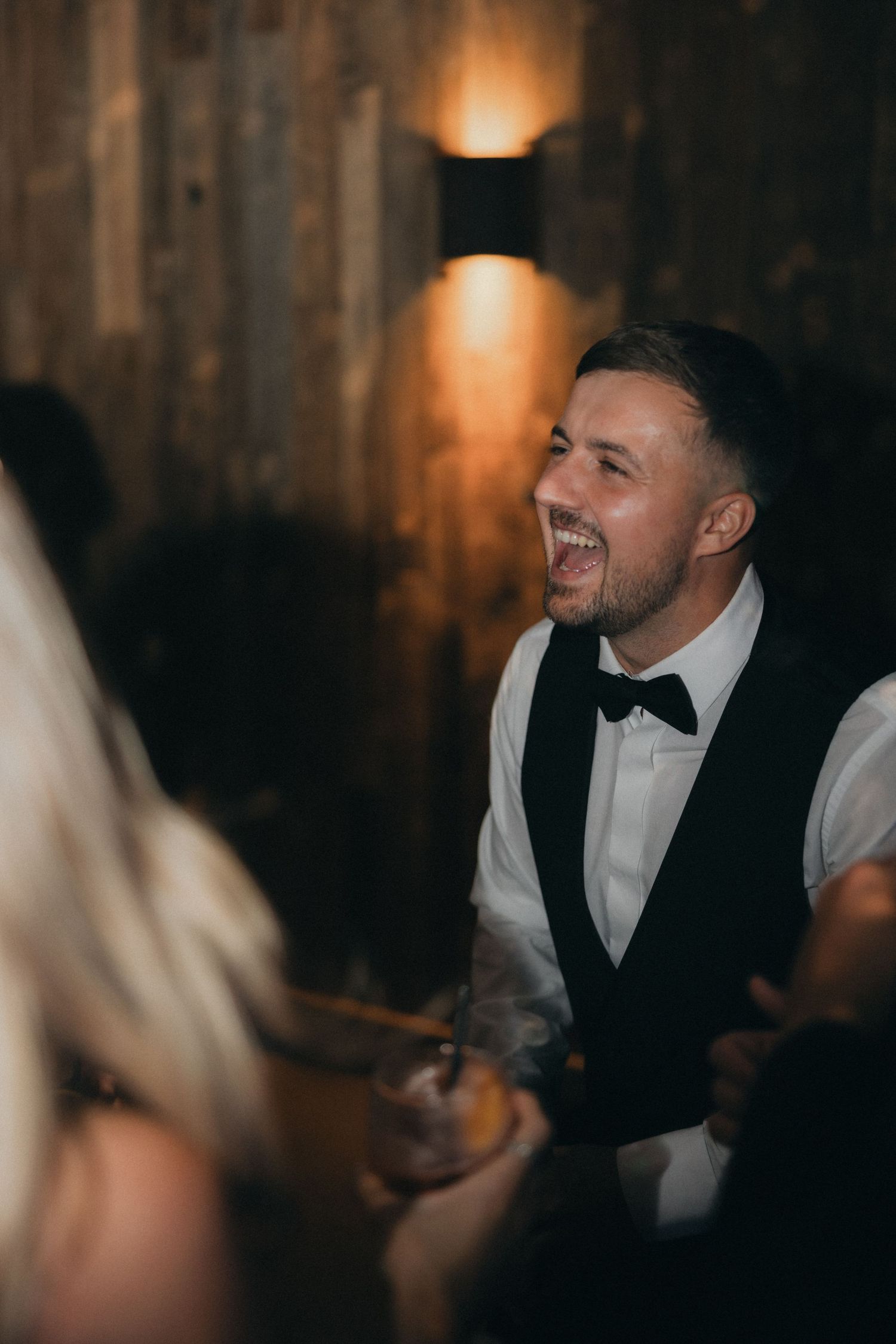Guest in formal attire smiles during wedding celebration.