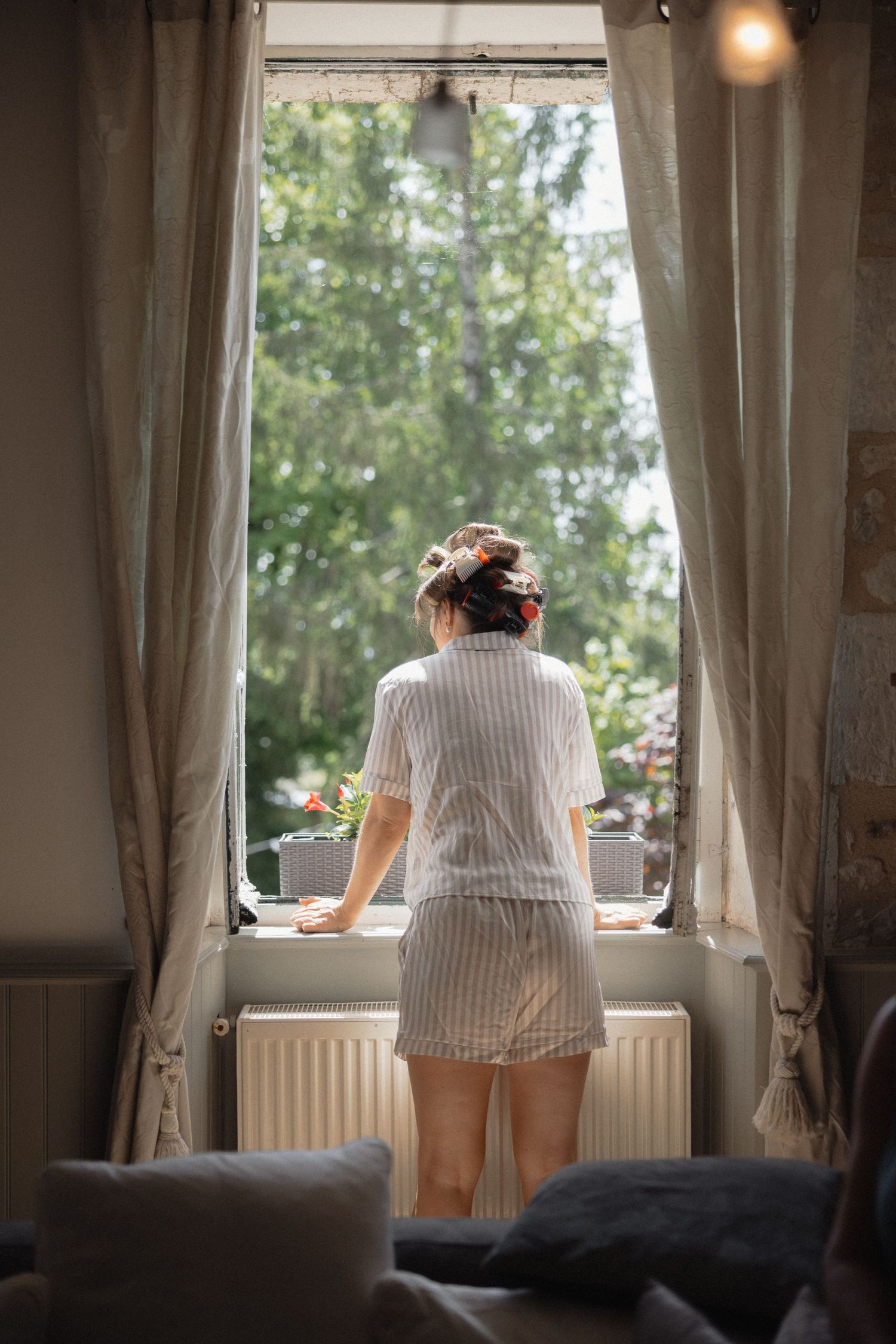 Person in striped shirt looking out window during wedding preparation.