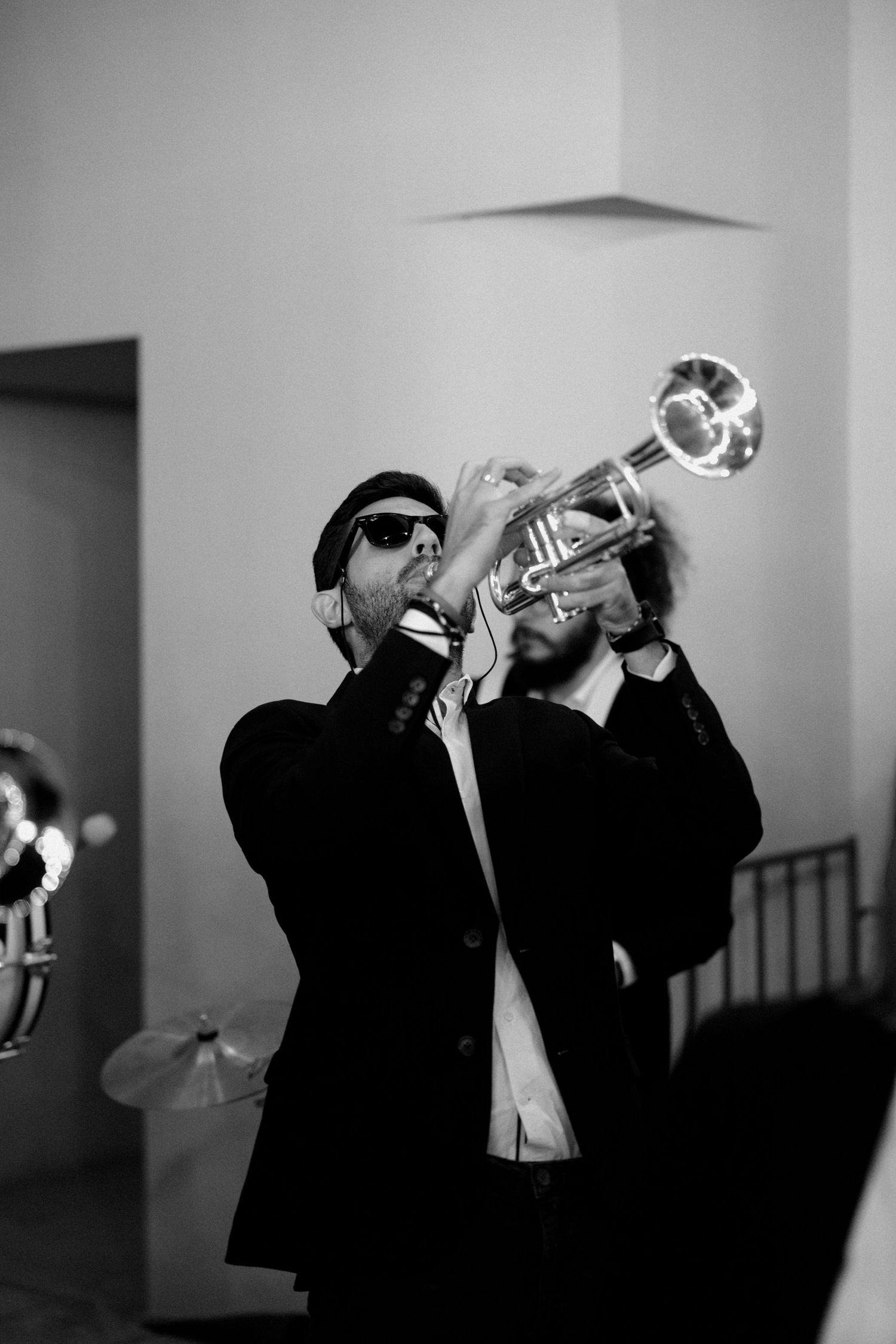 Musicians in black suits playing trumpets in dramatic black and white photography.
