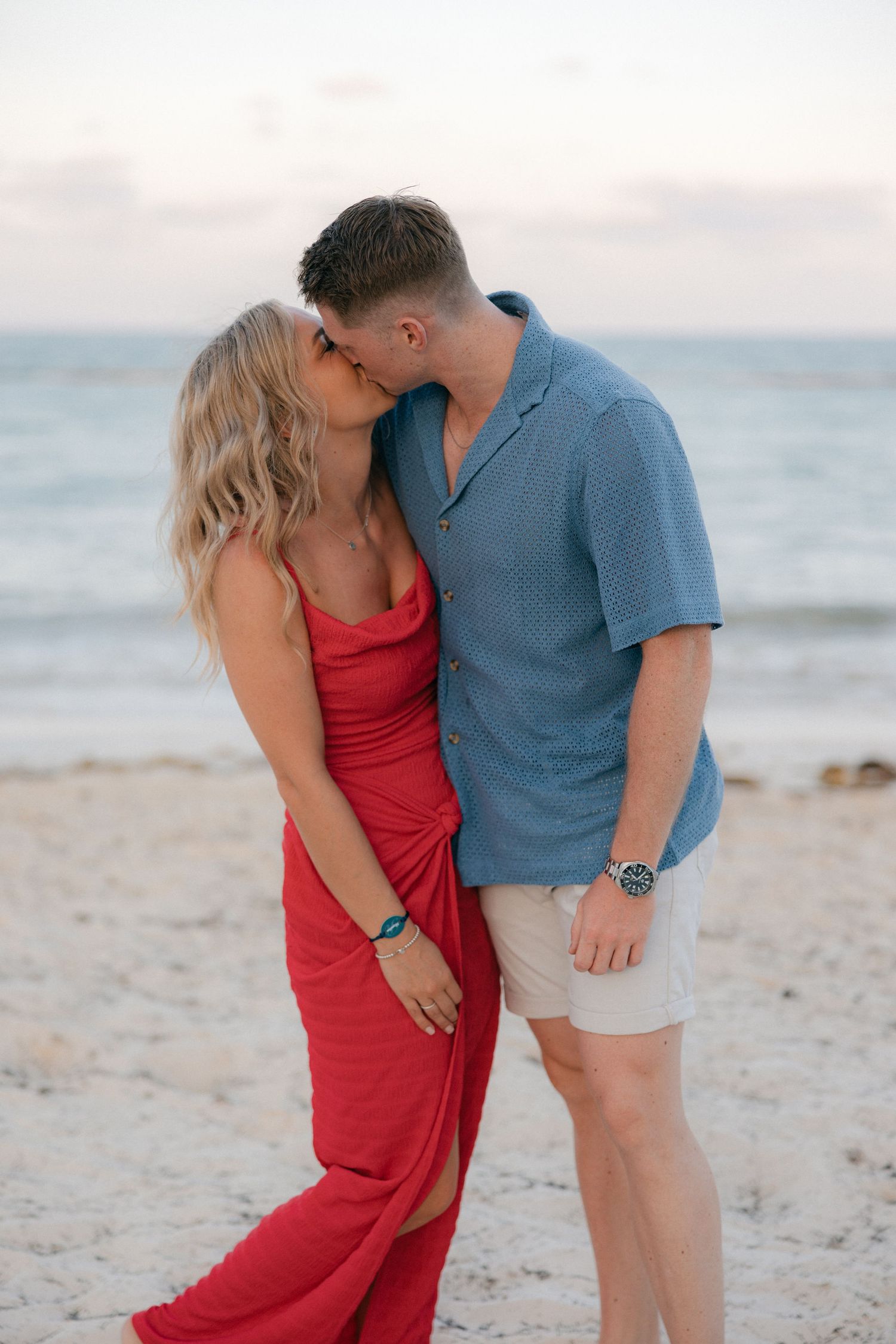A romantic couple embracing on a beach at sunset, with the woman wearing a flowing red dress.