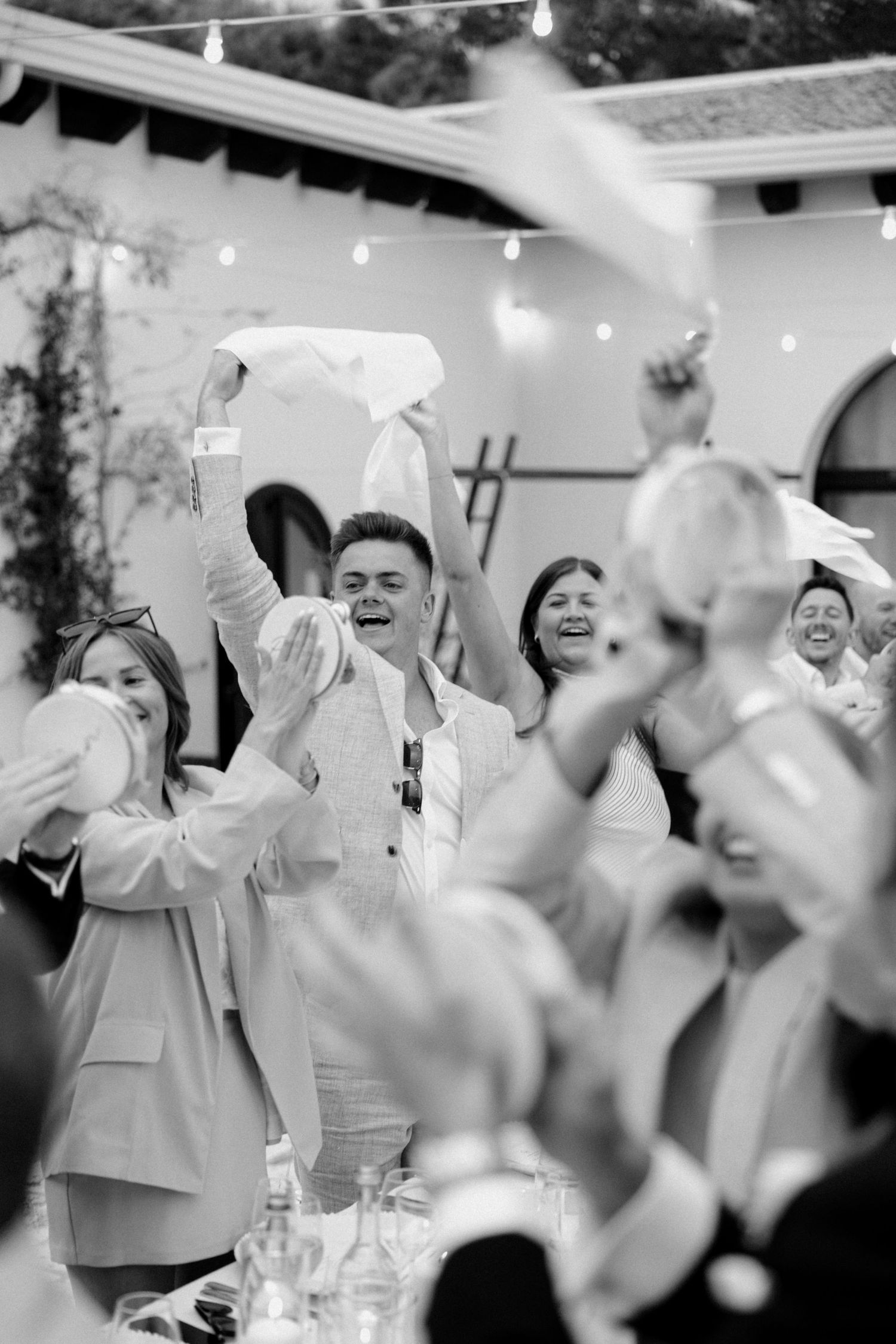 Black and white photo of wedding guests waving napkins during a celebration.