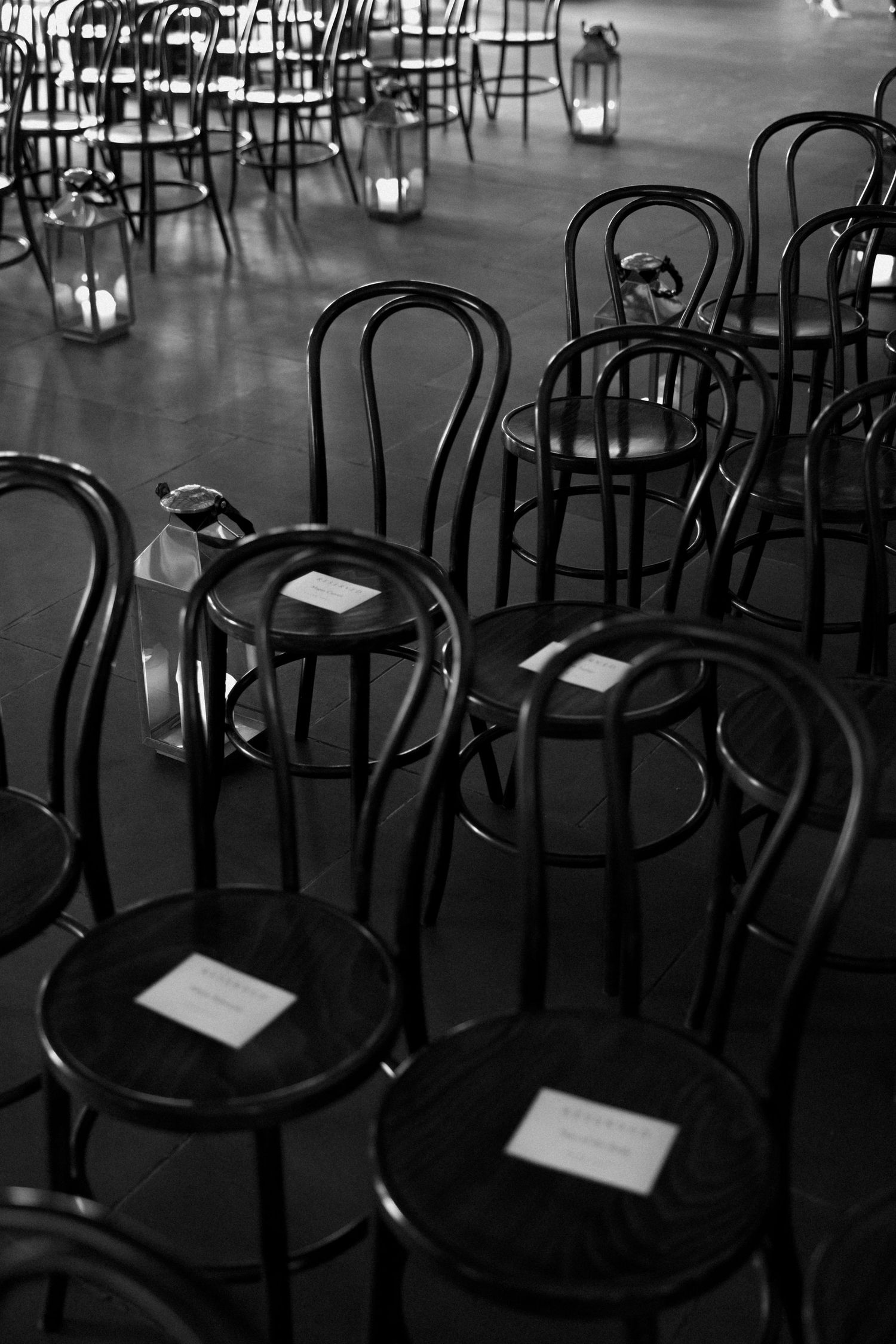 Black bentwood chairs arranged in rows with lanterns creating moody atmosphere.