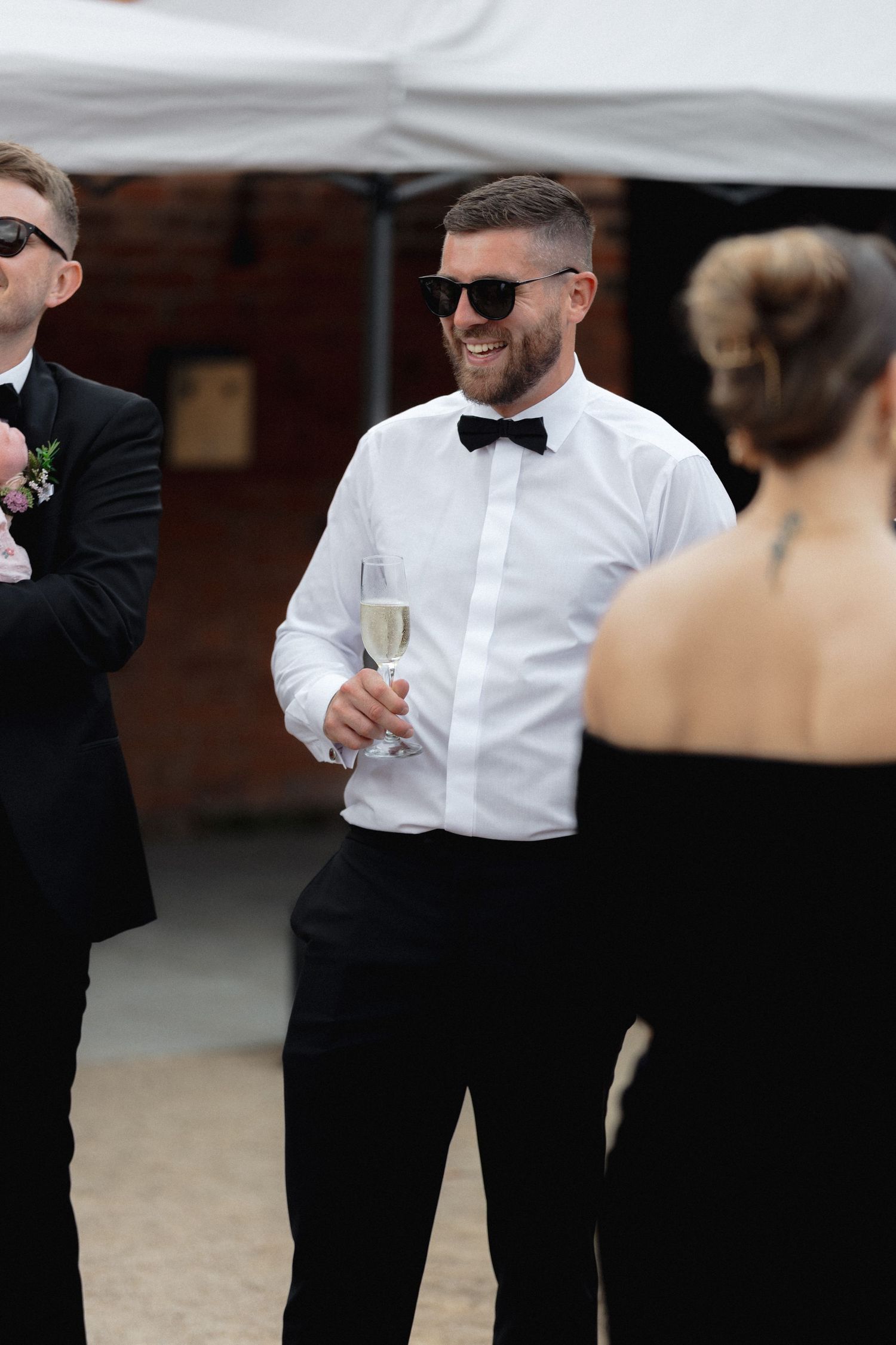 Wedding guests in formal black and white attire mingling outdoors.