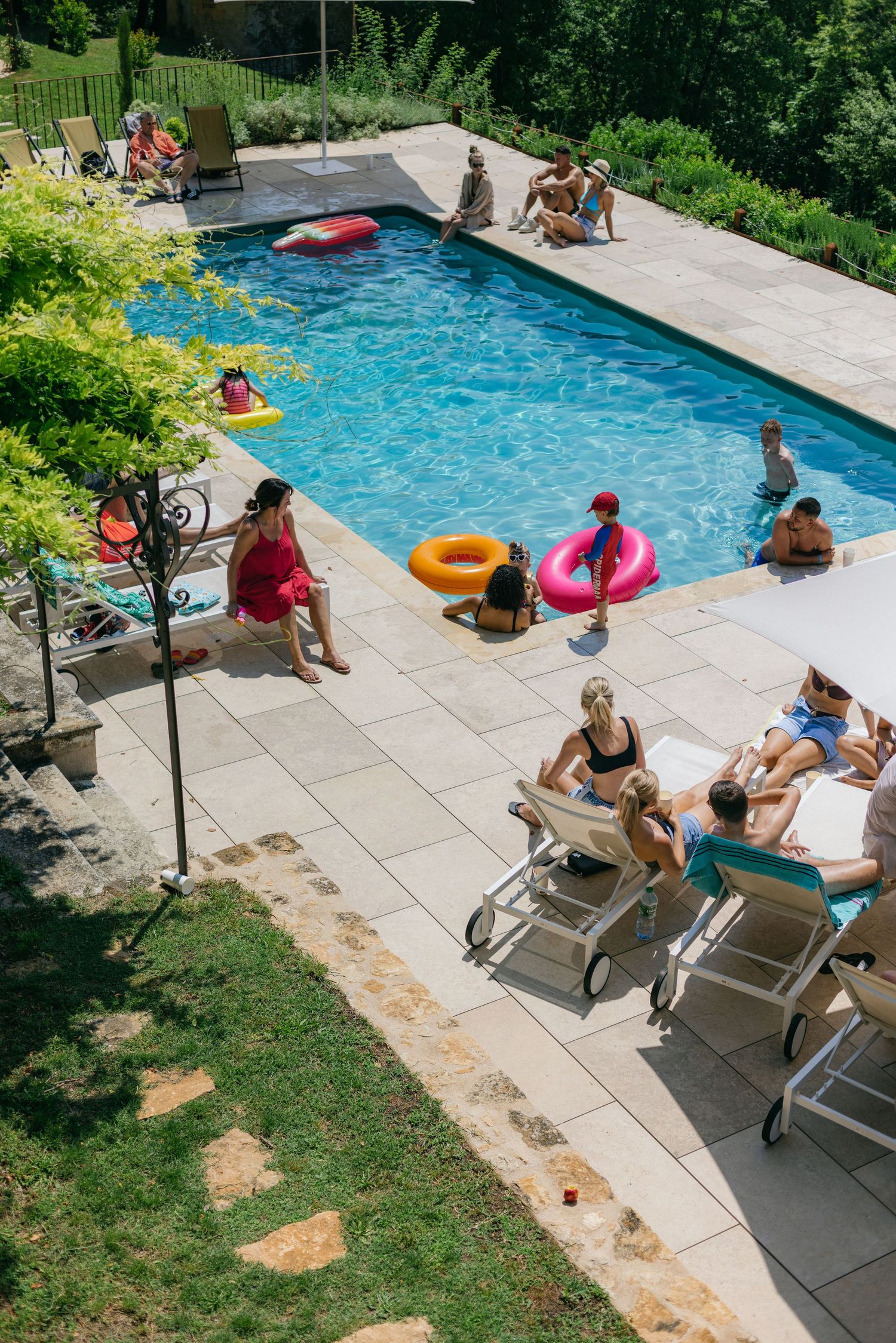 Friends enjoying a summer pool party with colorful floats and lounge chairs on a sunny day.