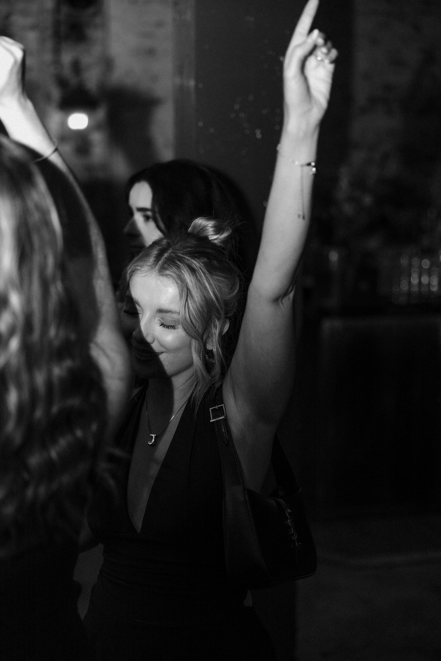 A black and white photo of a person dancing with their arms raised at a party.