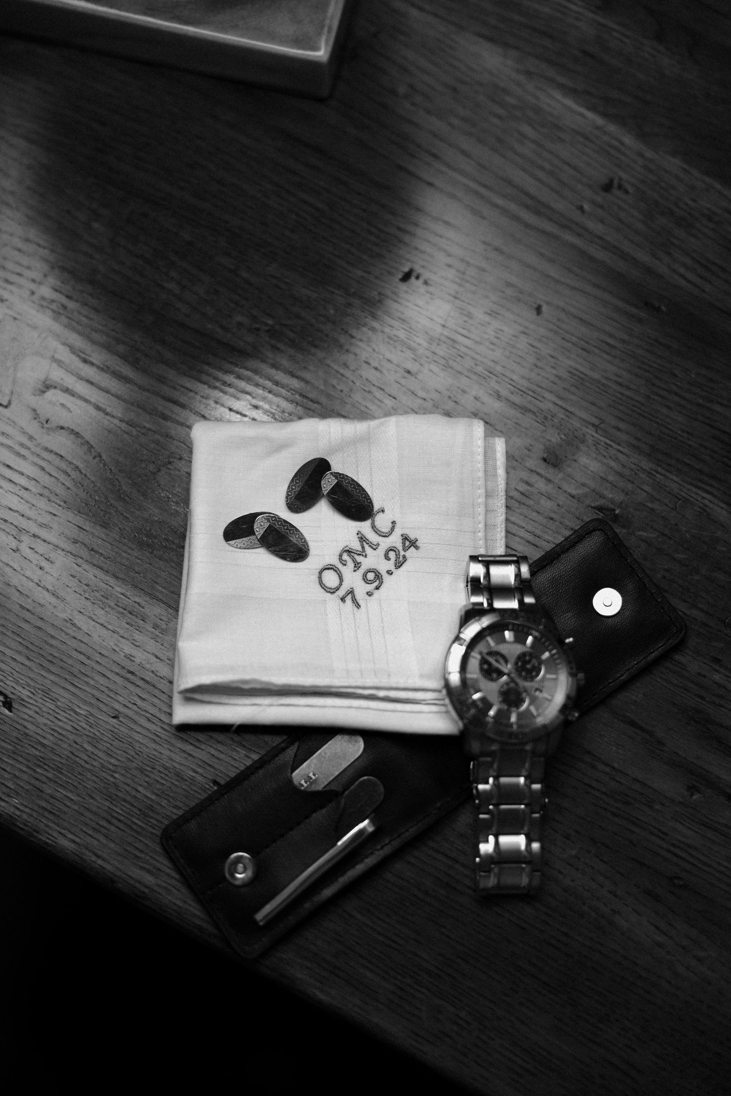 Black and white photo of watch and accessories on wooden surface.