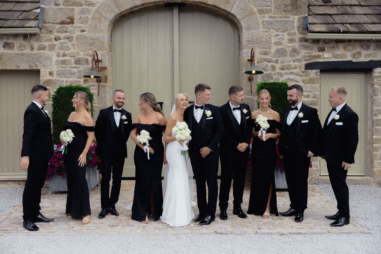 Wedding party poses in creative formation against rustic stone wall backdrop.