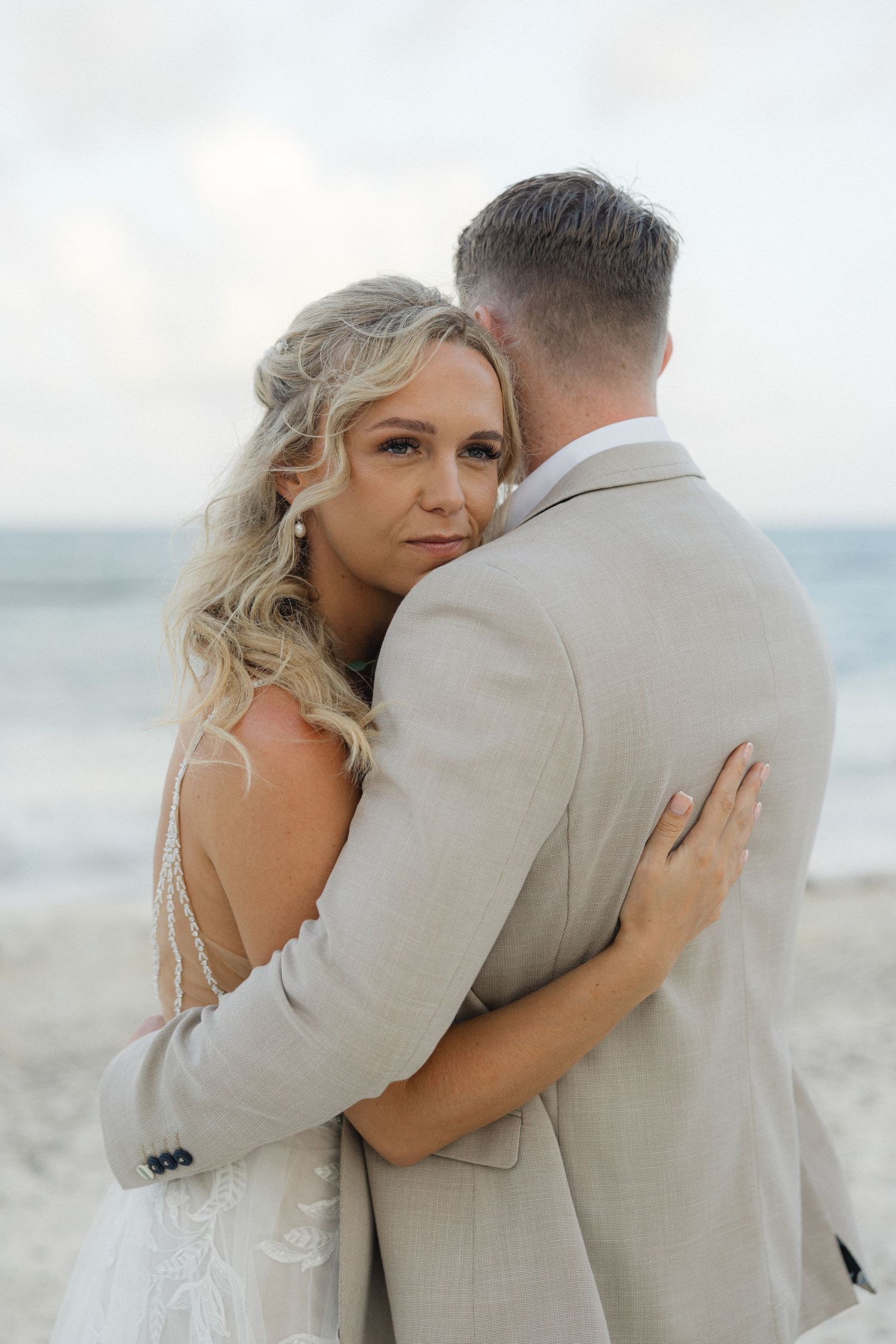 Wedding couple shares intimate moments on a sandy beach with waves in the background.