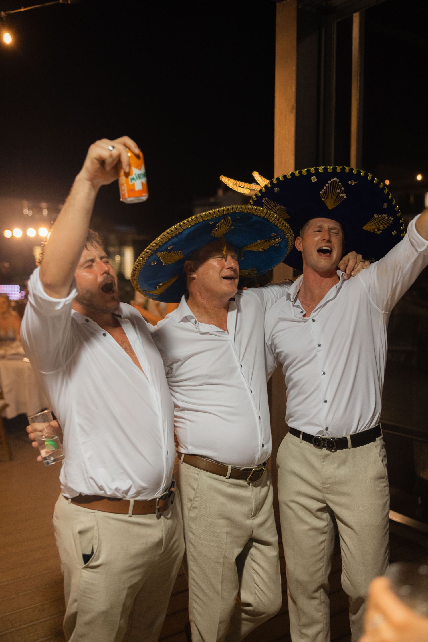 Group of guests in white shirts and khakis celebrating enthusiastically at nighttime party.