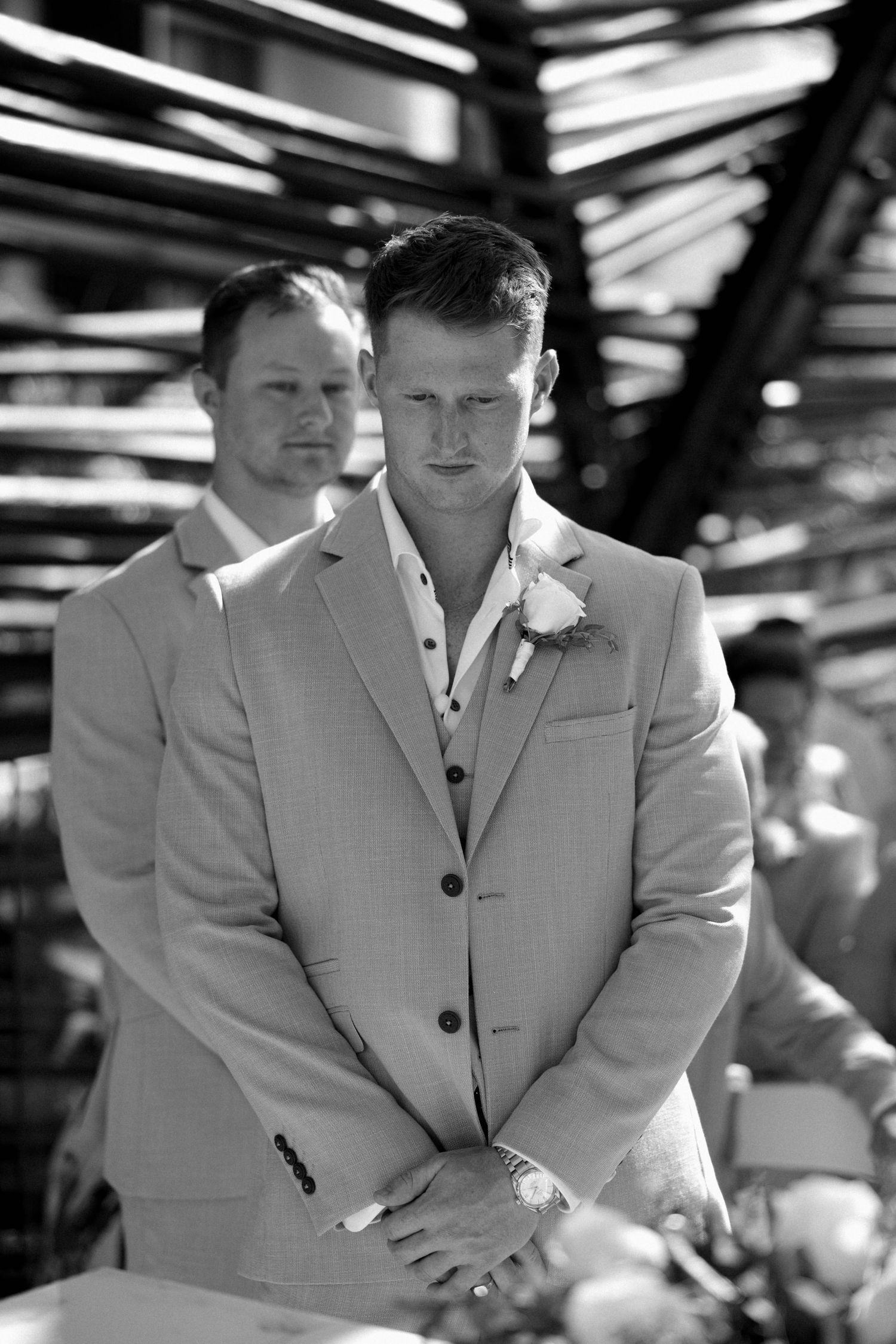 Wedding party members in light gray suits stand together during an outdoor ceremony.