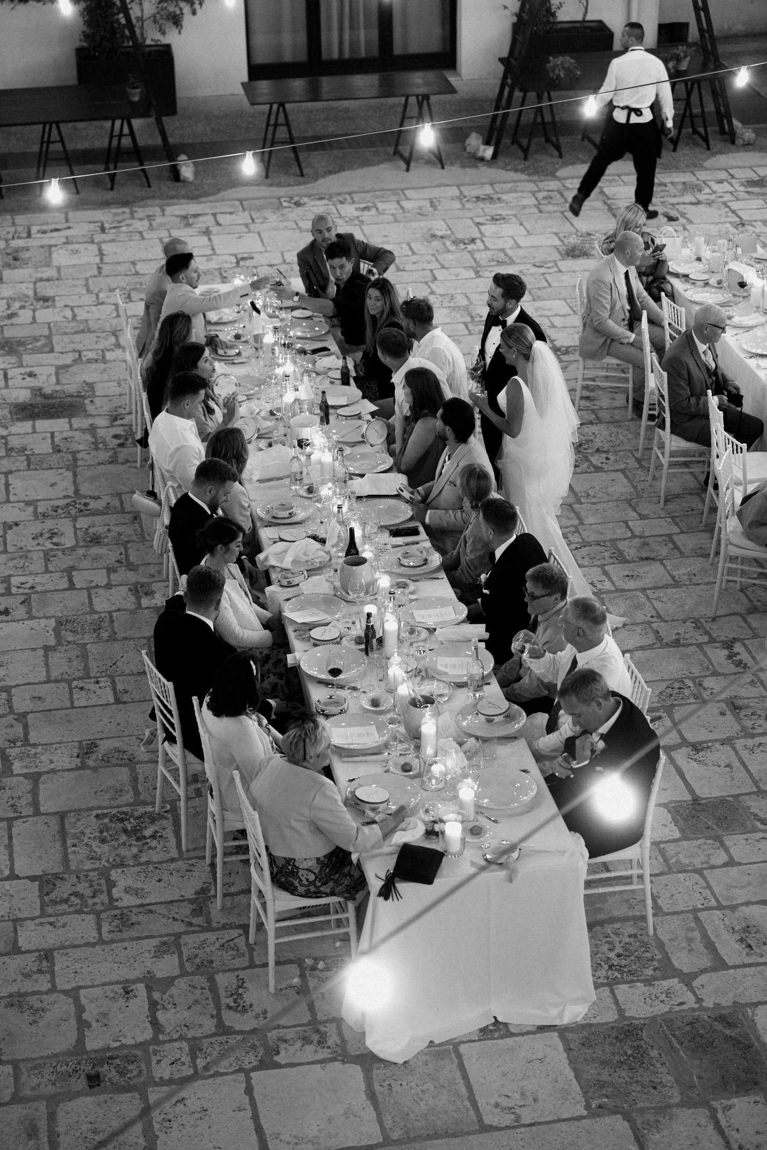 Black and white photo of wedding reception dinner with guests seated at illuminated tables.