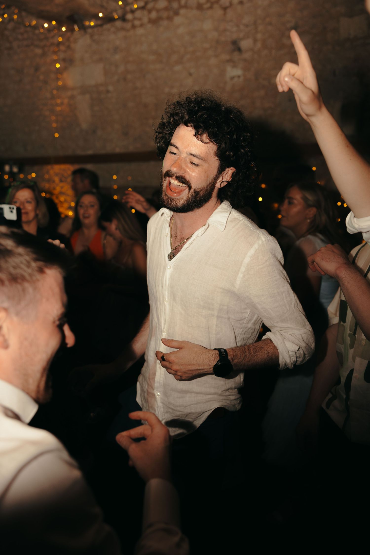 Party guest dancing and smiling at a celebration with string lights in background.