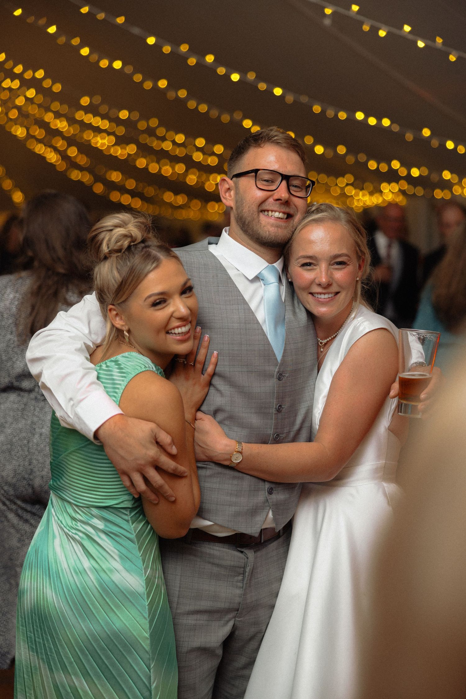 Wedding celebration with guests sharing emotional embraces under warm string lights.