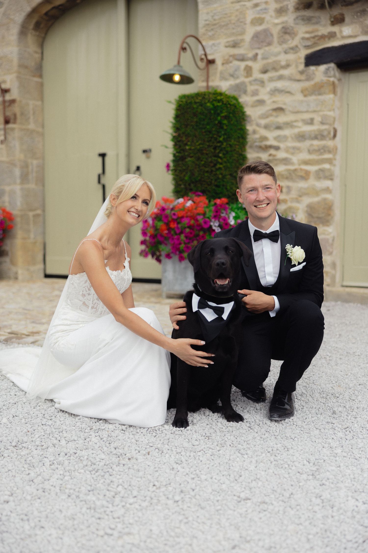 Wedding couple poses with black Labrador dog on stone patio.