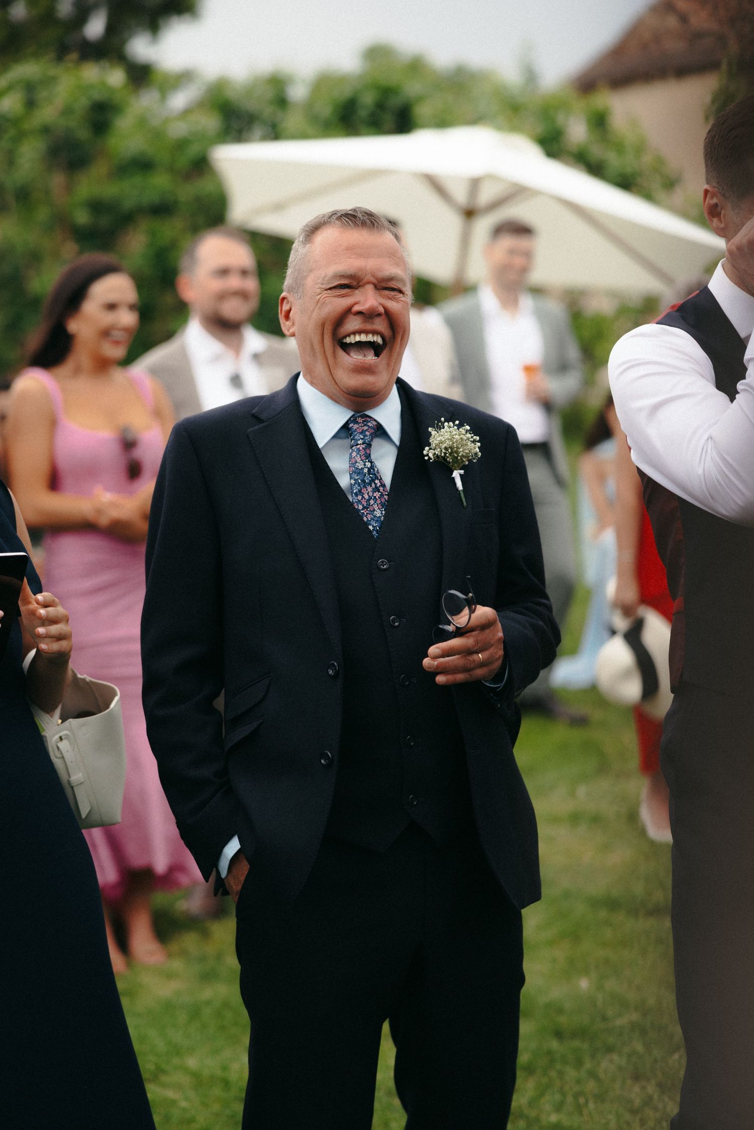 Wedding guests in formal attire sharing joyful laughter during outdoor reception.