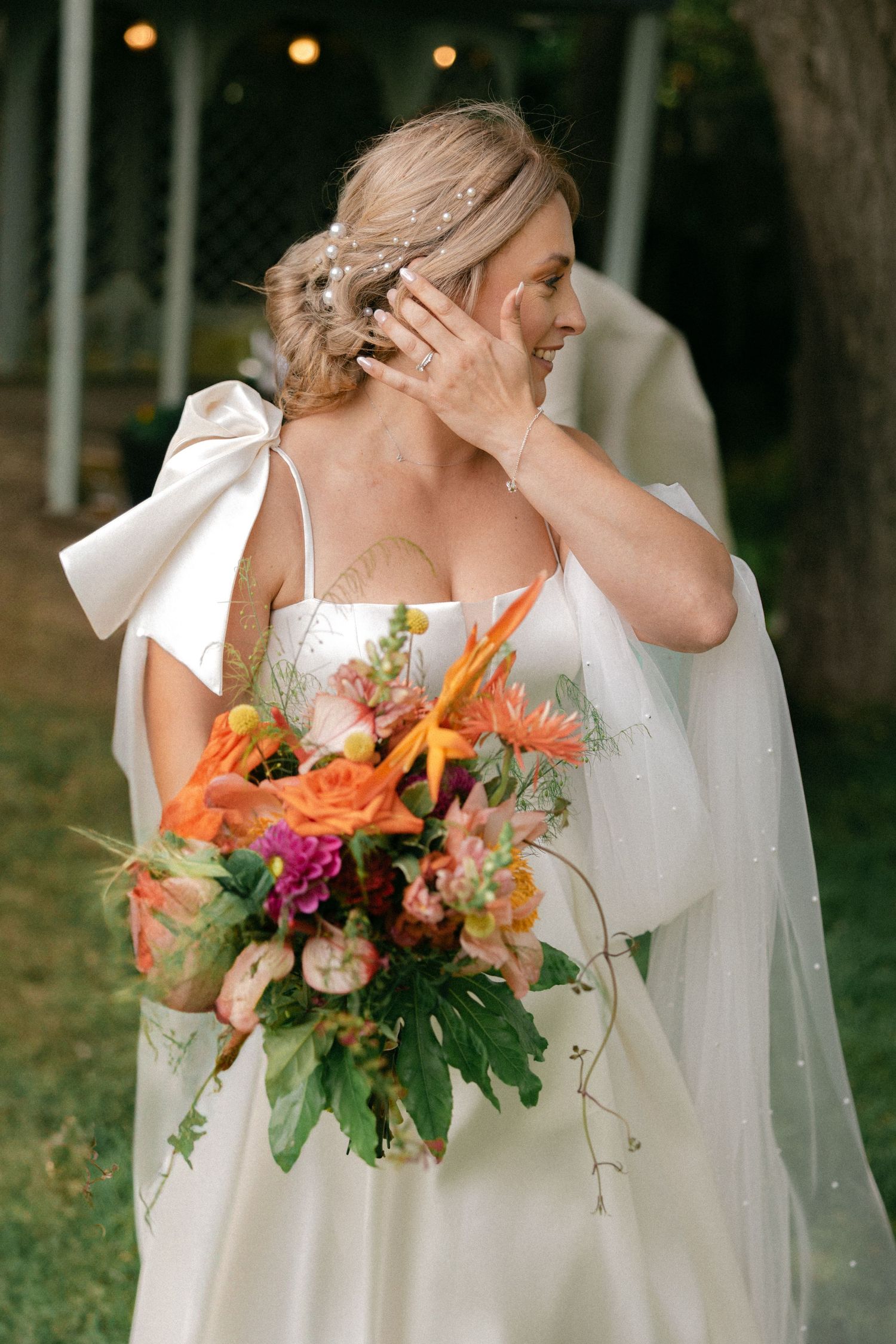 Emotional bride in white dress holding vibrant orange and pink bouquet outdoors.